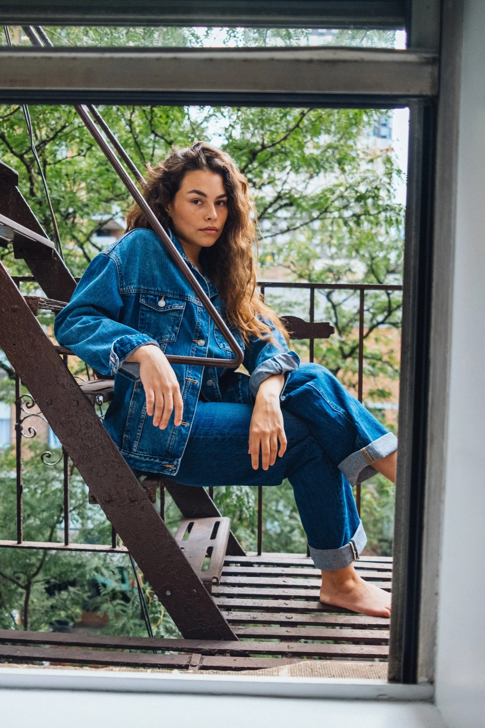 Model in a denim jacket and jeans seated on a city fire escape