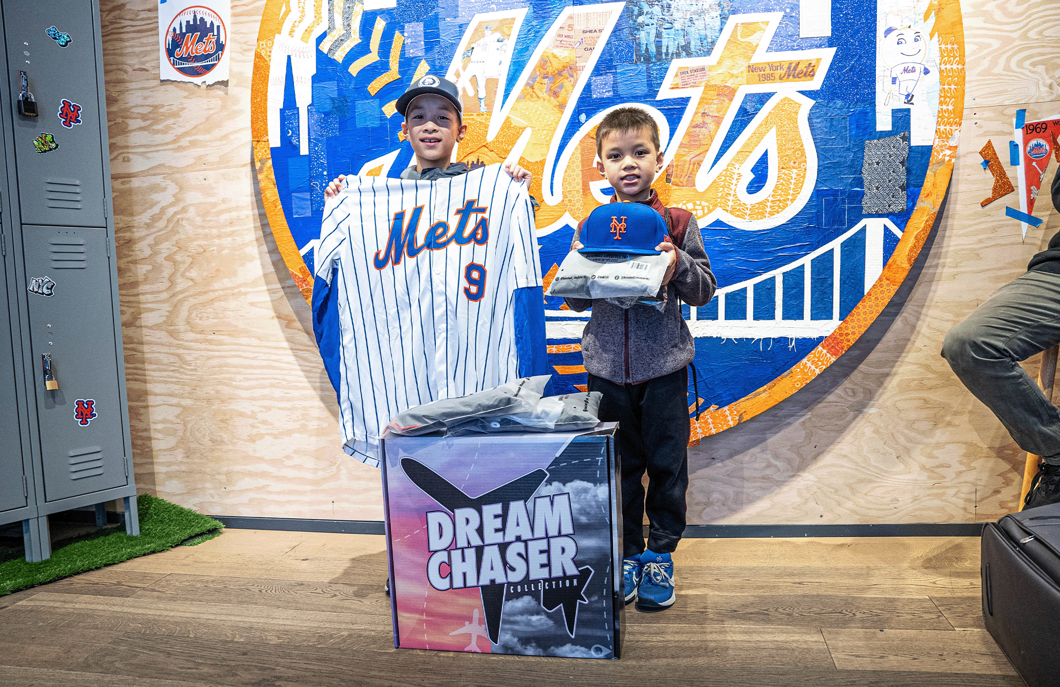 A GIF of Baseball Lifestyle 101 and NY Mets Dream Chaser Collection collab activation. The boy on the left holds a Mets jersey, and the boy on the right holds a Mets cap and a package. There are lockers and decorations with Mets logos around them.