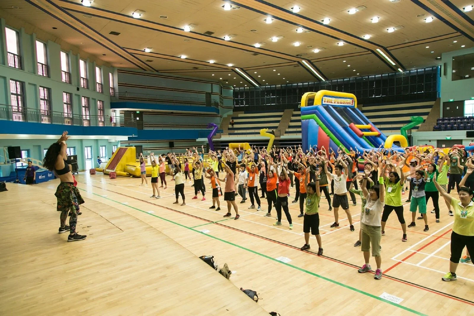 People participating in a group exercise class in an indoor gymnasium with inflatable slides in the background.