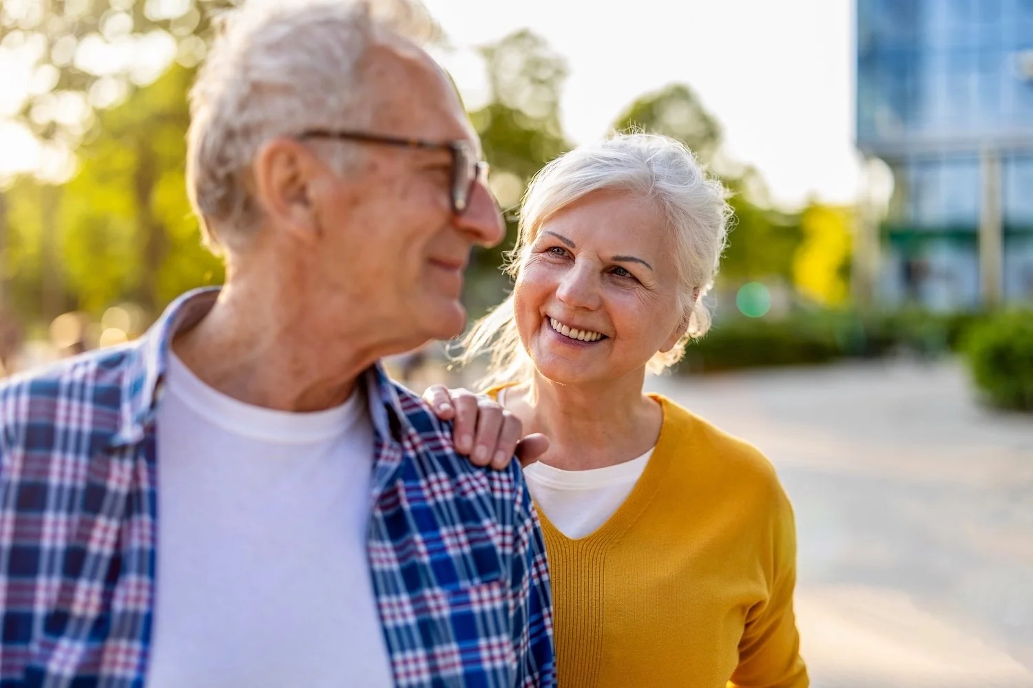 Iäkäs iloinen pariskunta ulkona ja naisen käsi miehen olkapäällä.