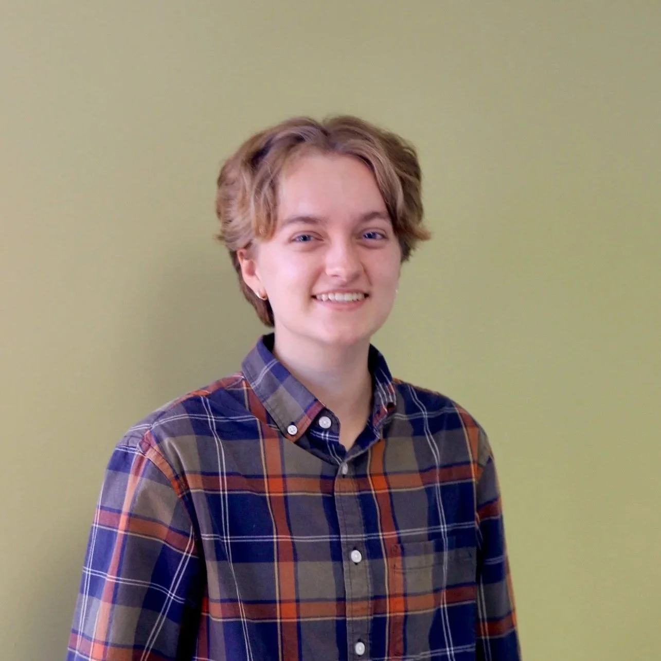 Person in a plaid shirt standing against a light green wall.