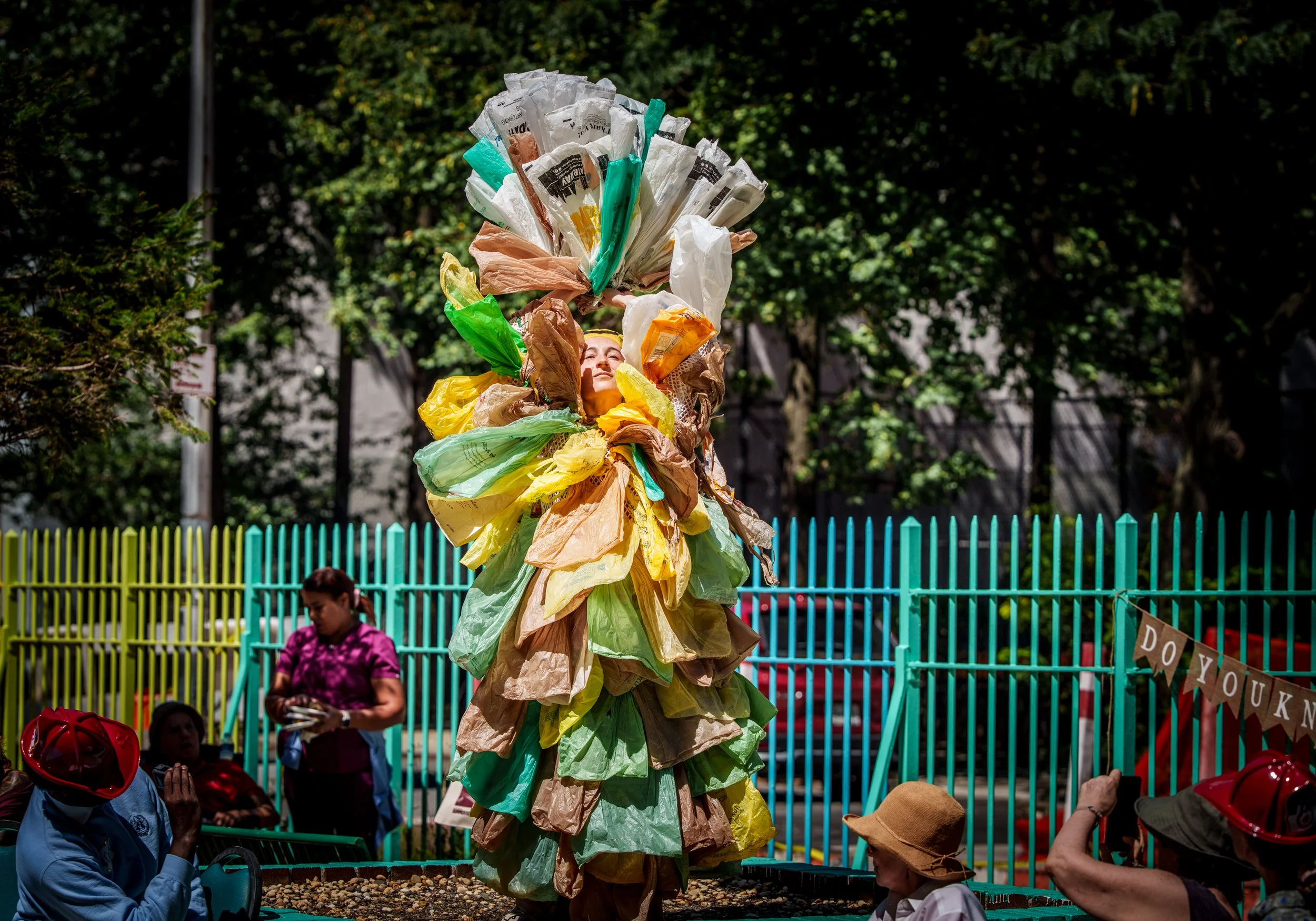 Dancer in plastic bag costume standing in a garden bed.