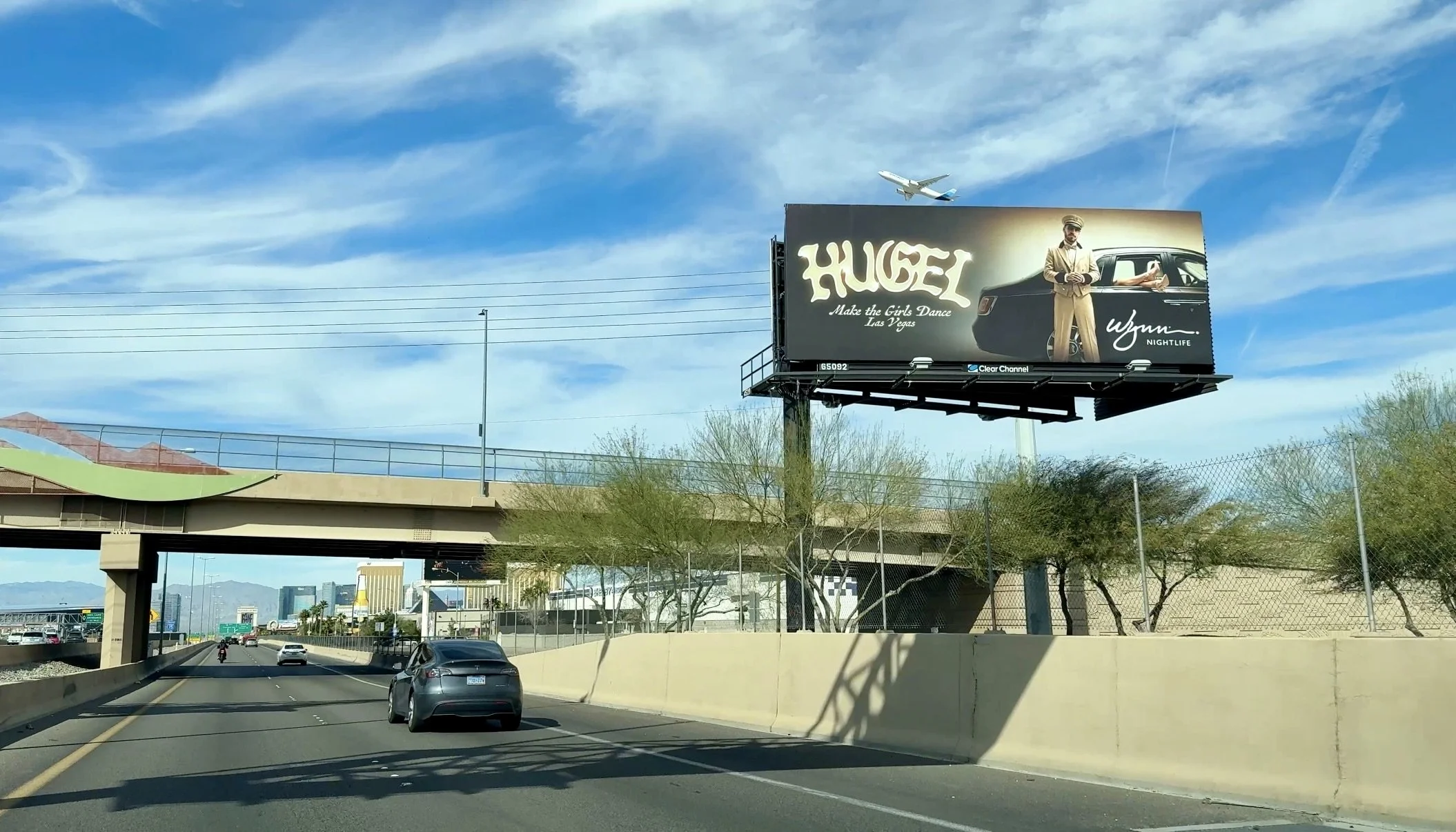 Street-level digital spectacular featuring Hugel. The creative leans into a "Poster-Art" style, blending Latin-house warmth with the sleek, high-end branding of Wynn Nightlife.