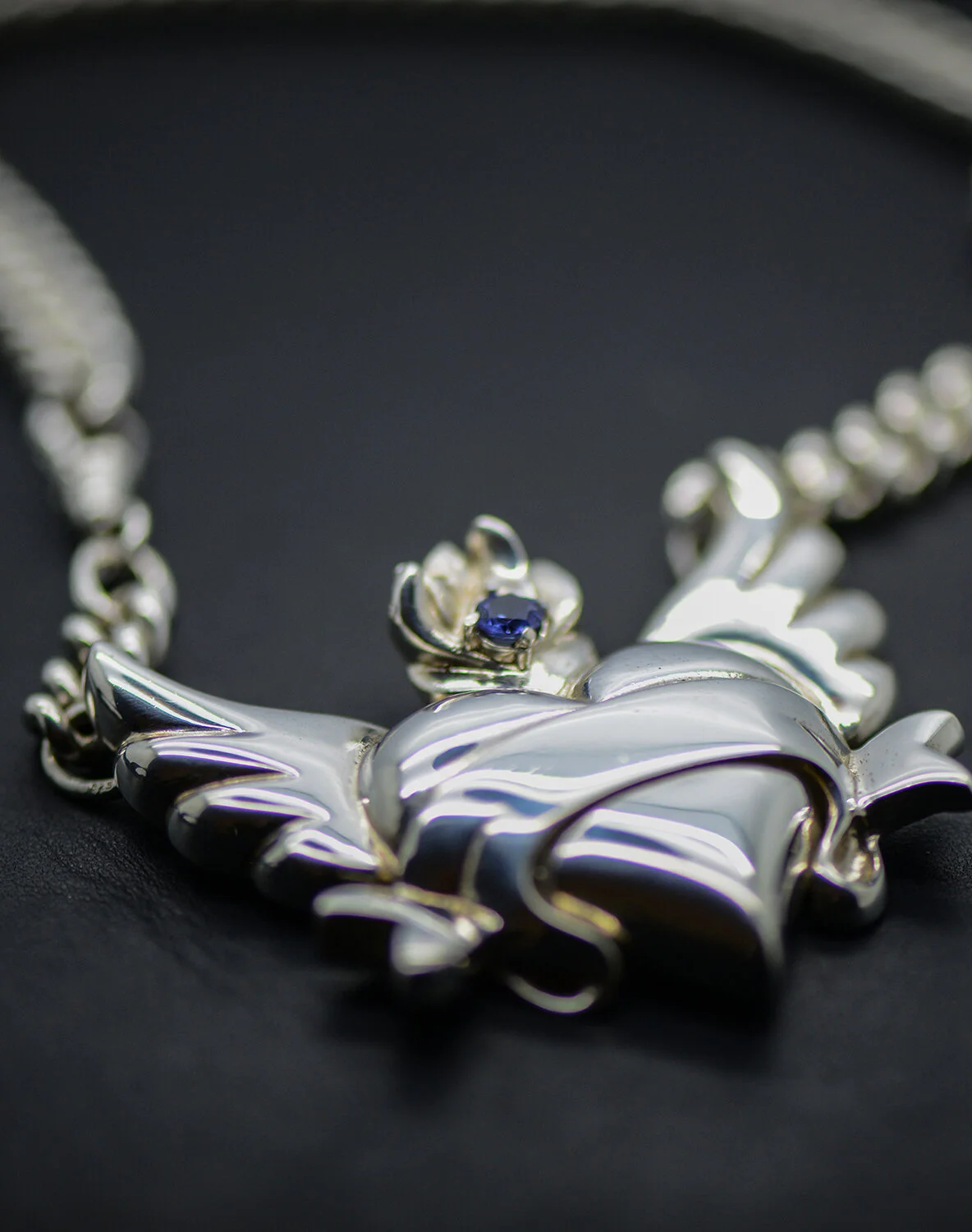 Close up winged heart with ribbon scroll set with blue sapphire. Statement necklace