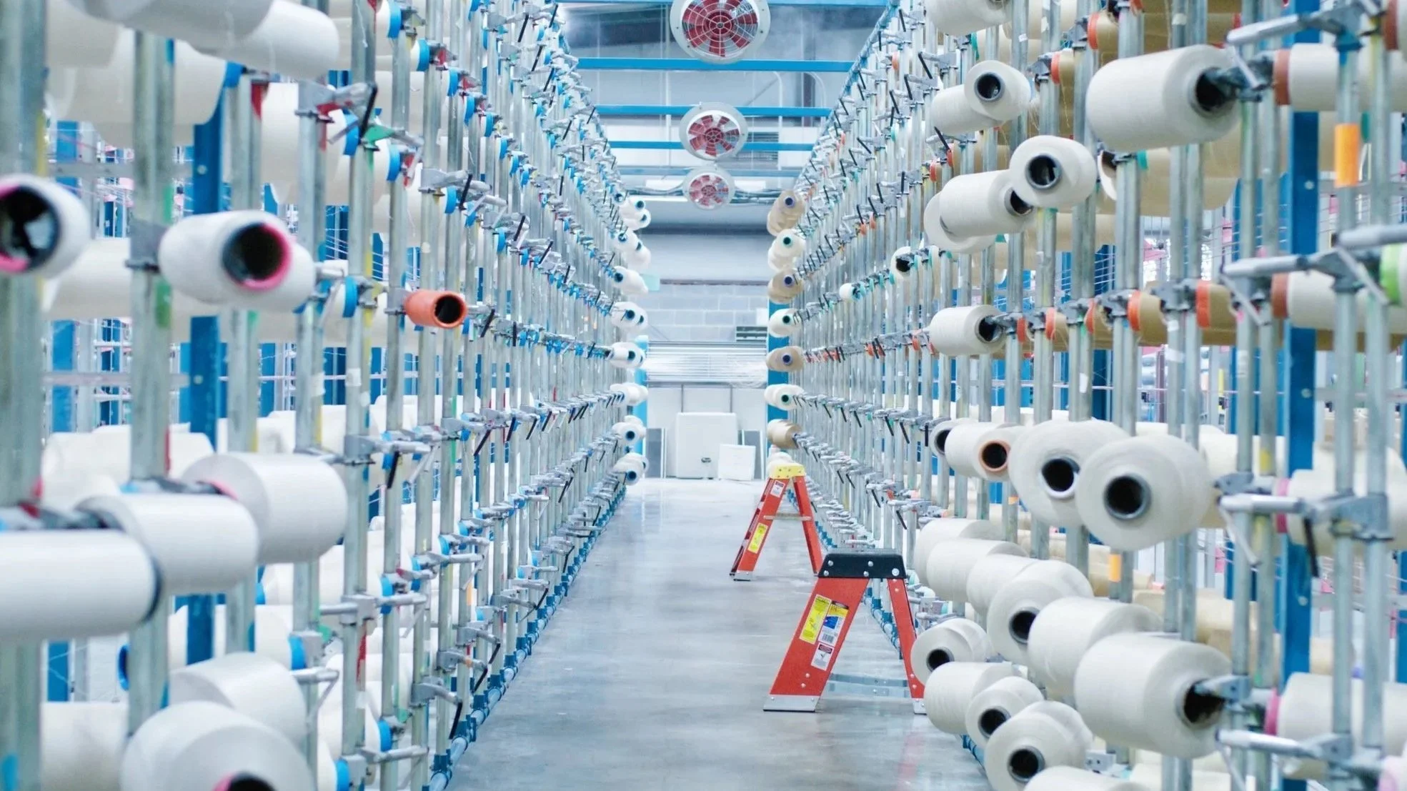 Rows of white thread spools inside a textile manufacturing facility for Revolution Performance Fabrics.