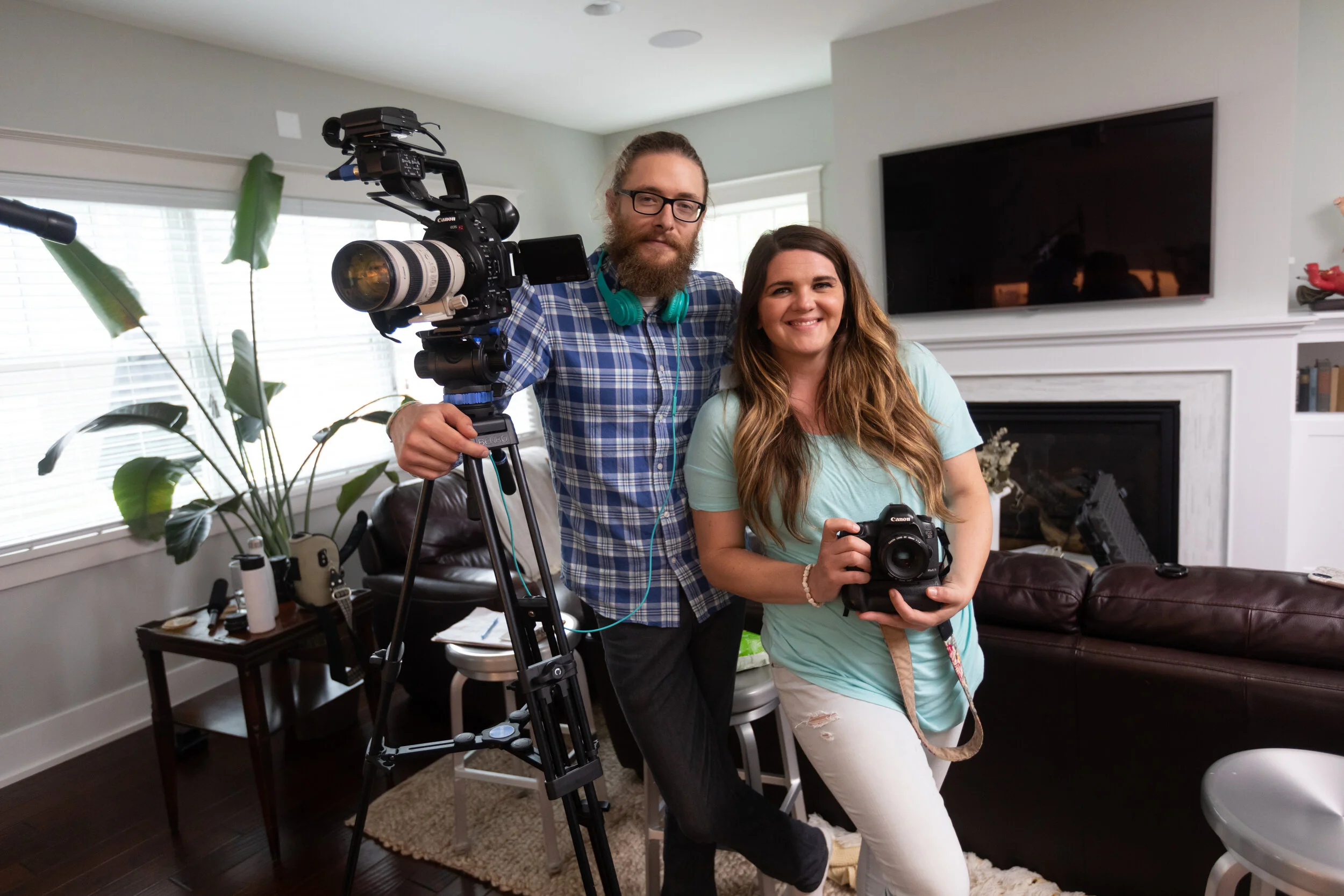 Two people, a man and a woman, at home, with cameras and a tripod, smiling for the photo.