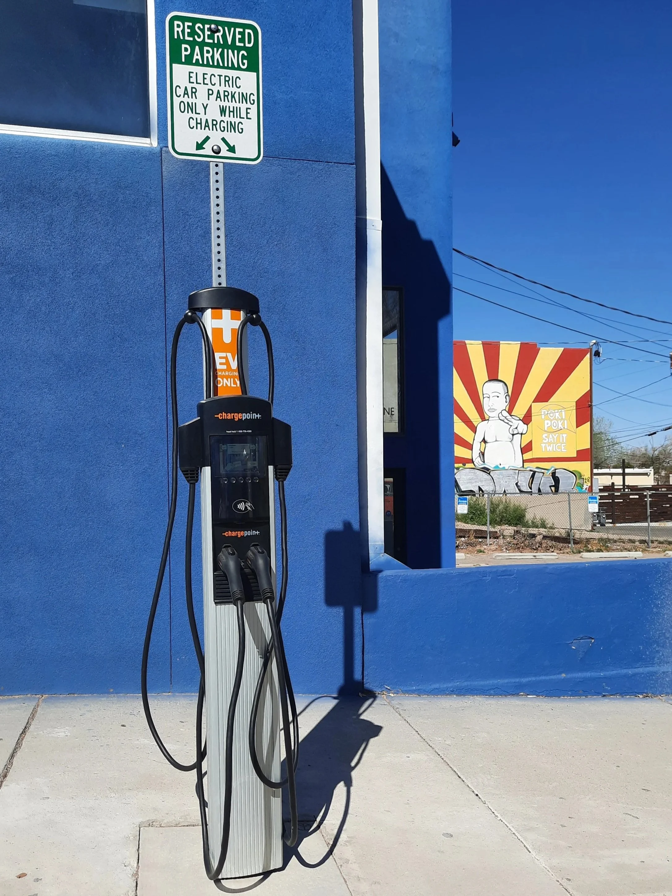 Electric vehicle charging station outside a blue building in Nob Hill with a sign indicating reserved parking for electric cars only while charging. There is a colorful mural on a wall in the background.