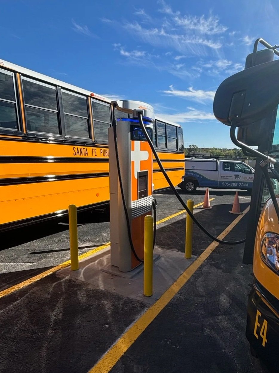 Electric vehicle charging station with a school bus parked nearby in a parking lot under a blue sky in Santa Fe.