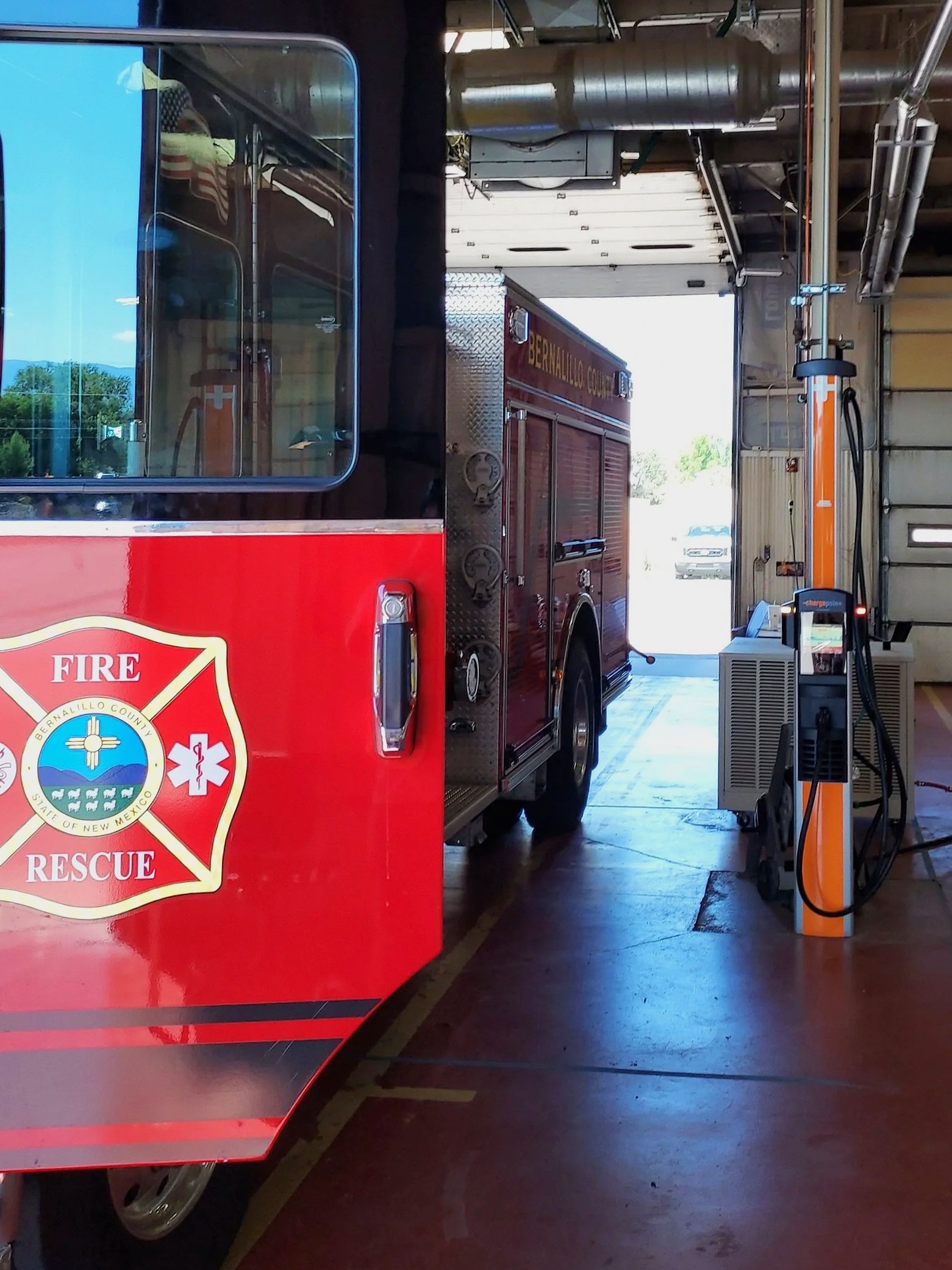 A fire truck with the logo of Bernalillo County Fire Rescue inside a garage, and an electric vehicle charging station on the right.