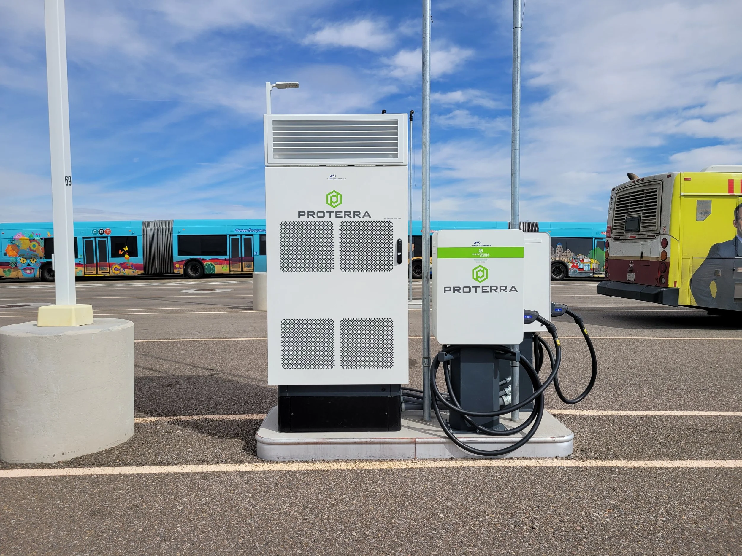 Electric vehicle charging station in a parking lot with an Albuquerque city bus in the background, and a clear blue sky.