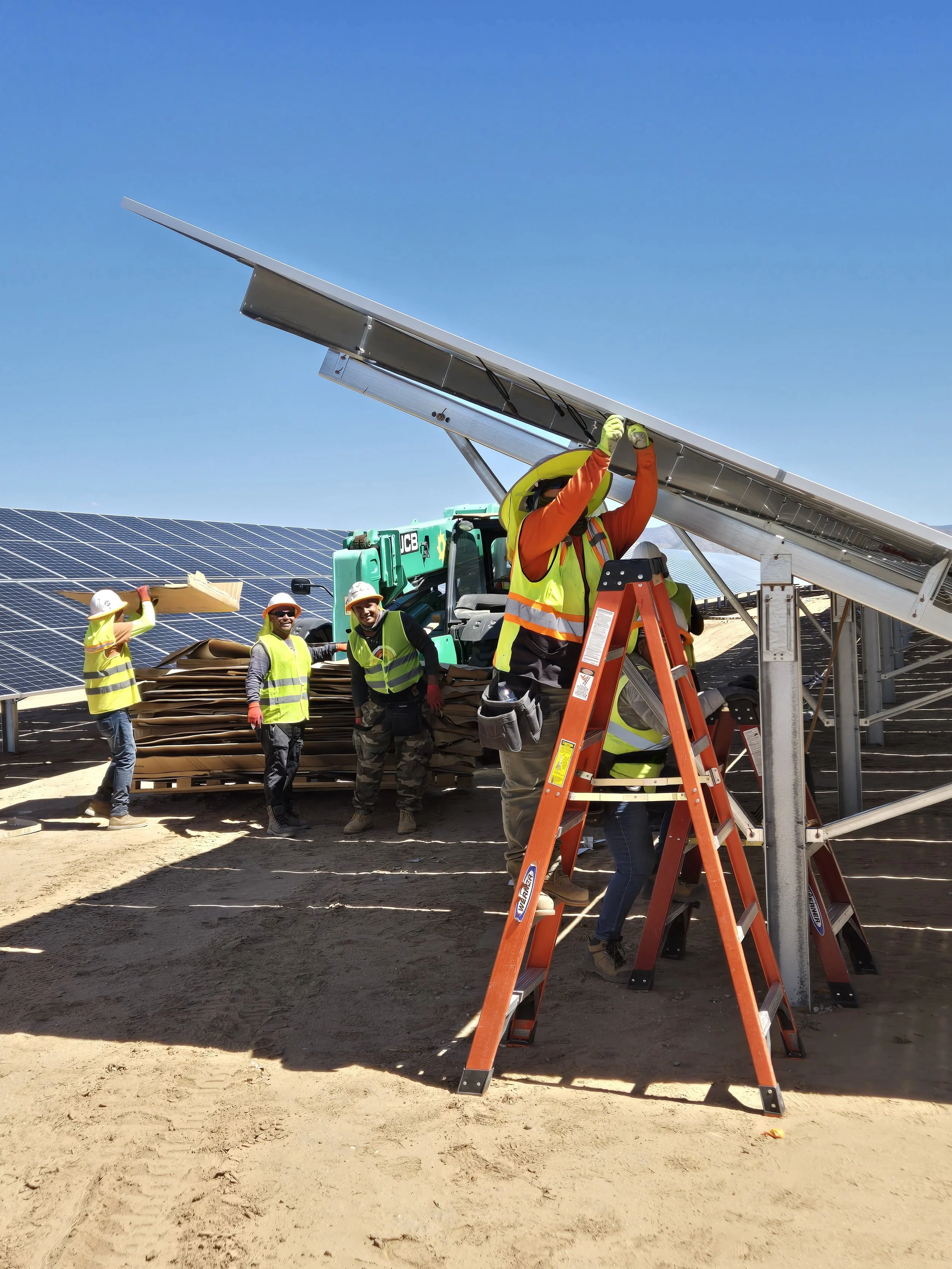 Workers installing solar panels on a sunny day, with some on ladders and others handling solar panels in a field.