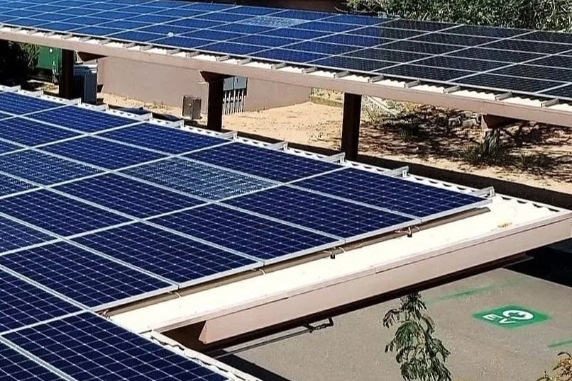 Close-up of solar panels installed on a solar parking canopy roof with electric vehicle charging in the parking lot below.