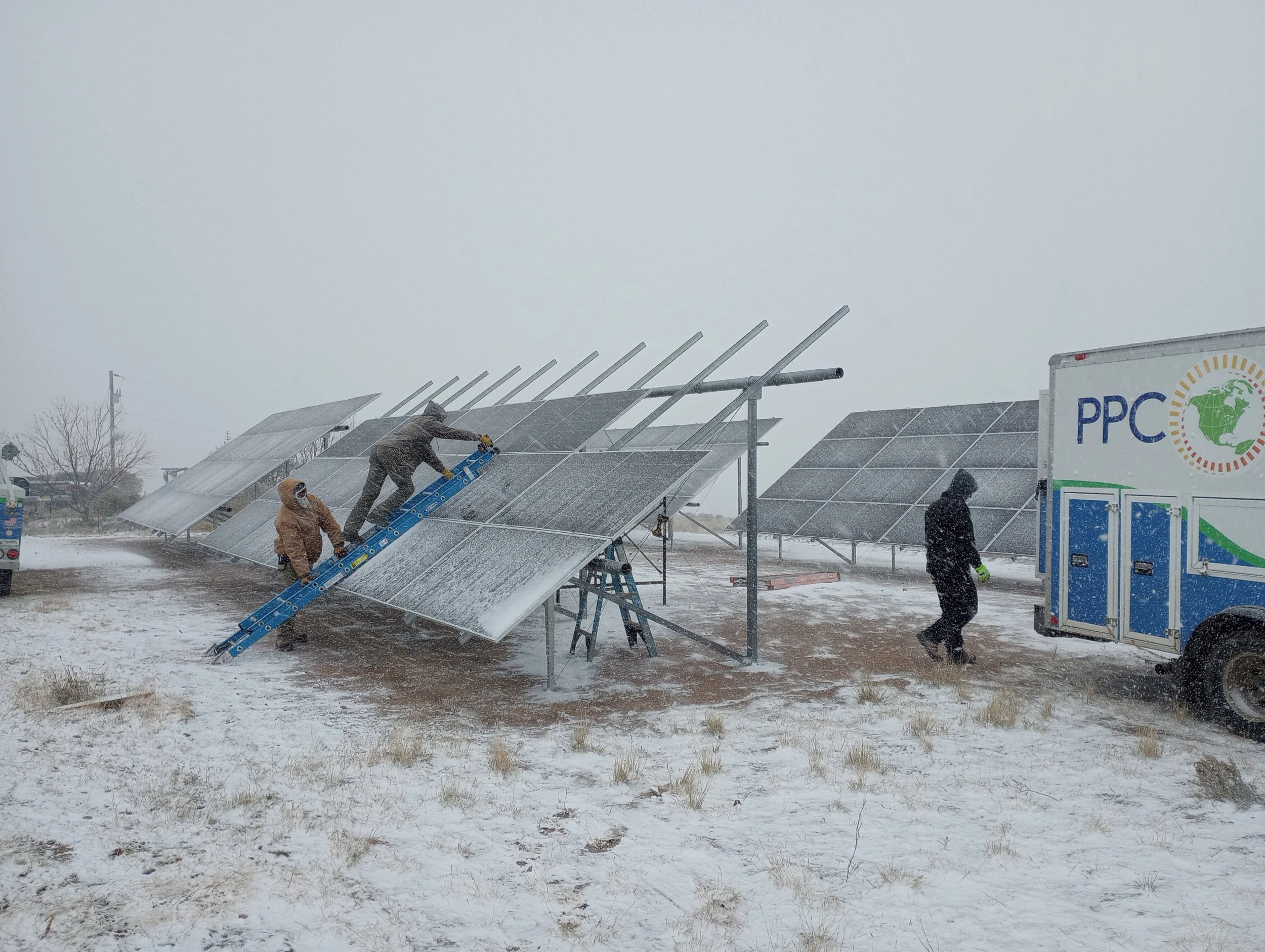 People installing solar panels on a cloudy, snowy day with a truck labeled PPC and a logo of a globe.