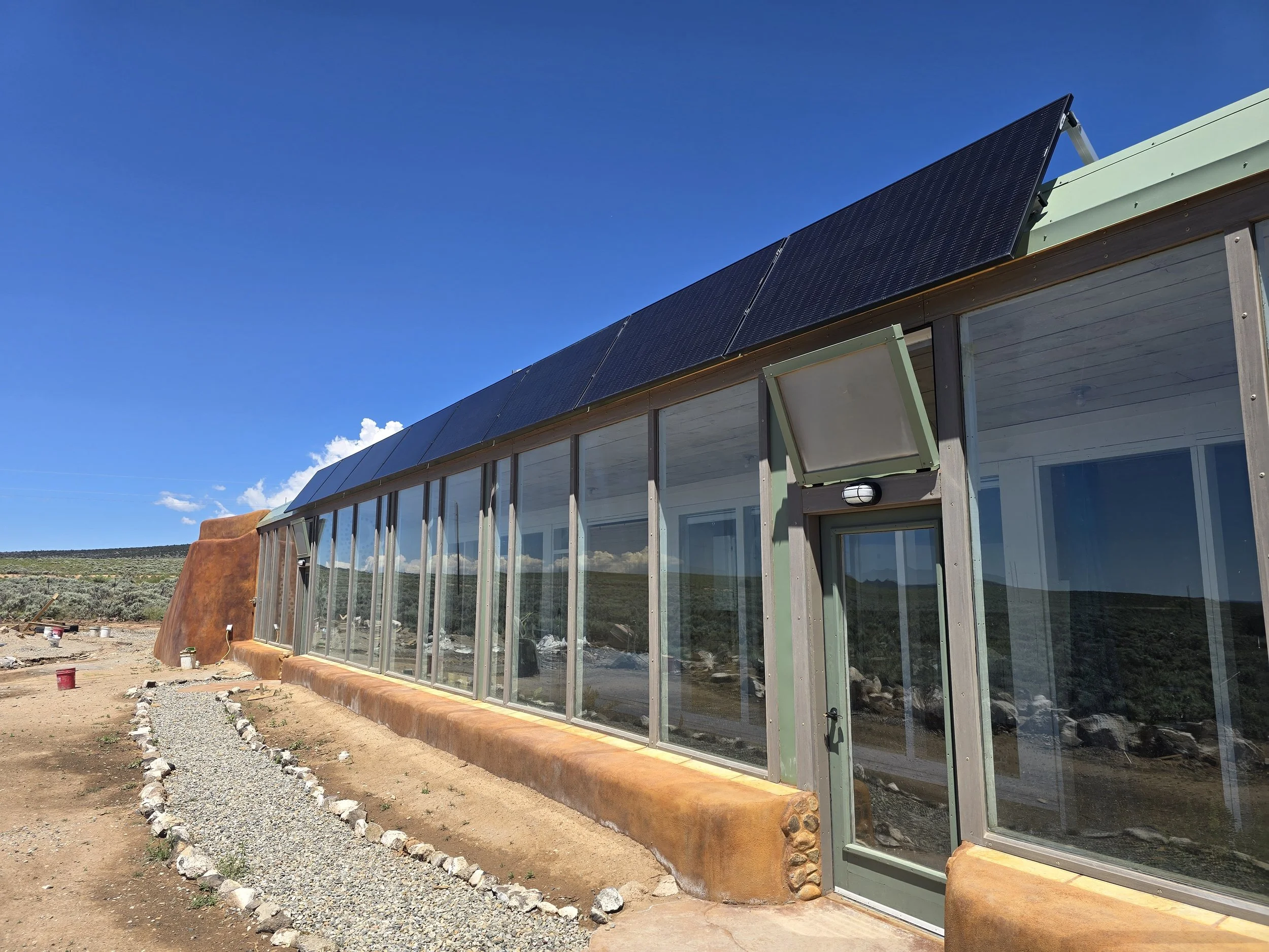 A row of solar panels installed on the roof of an off grid home, against a blue sky.