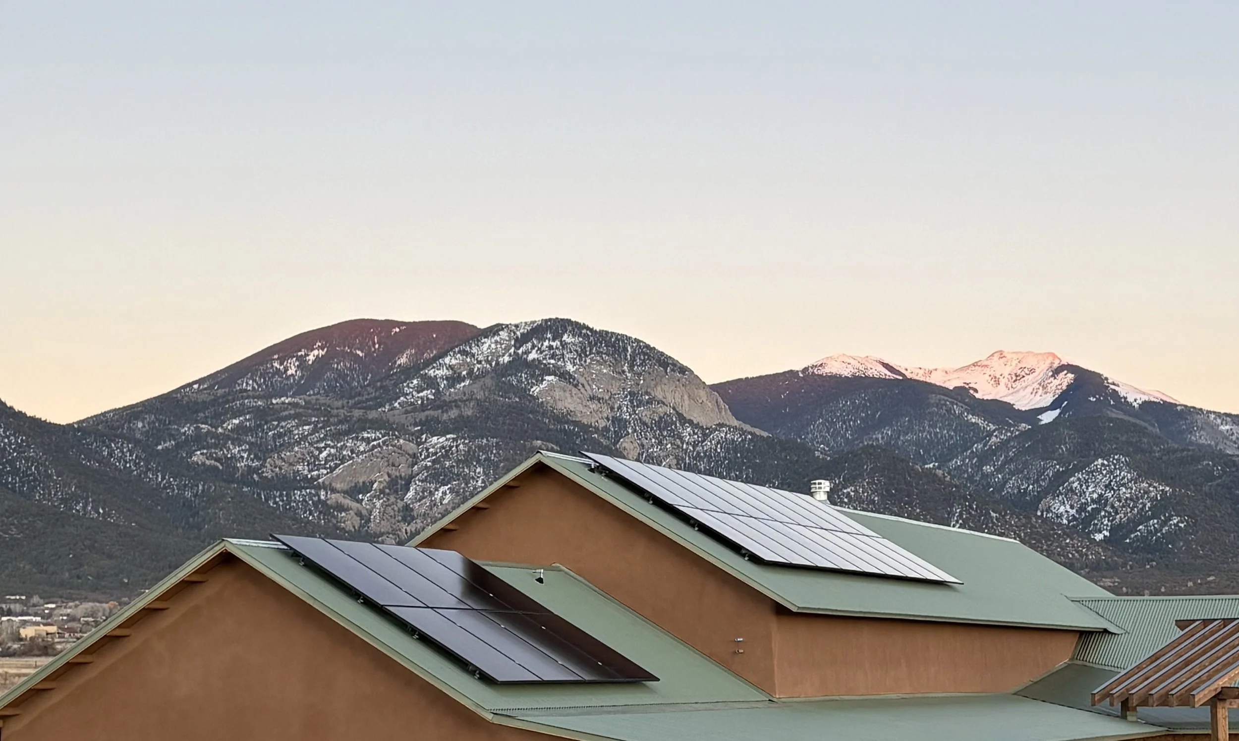 A house with solar panels on the roof in front of mountainous landscape with snow-capped peaks in Taos New Mexico.