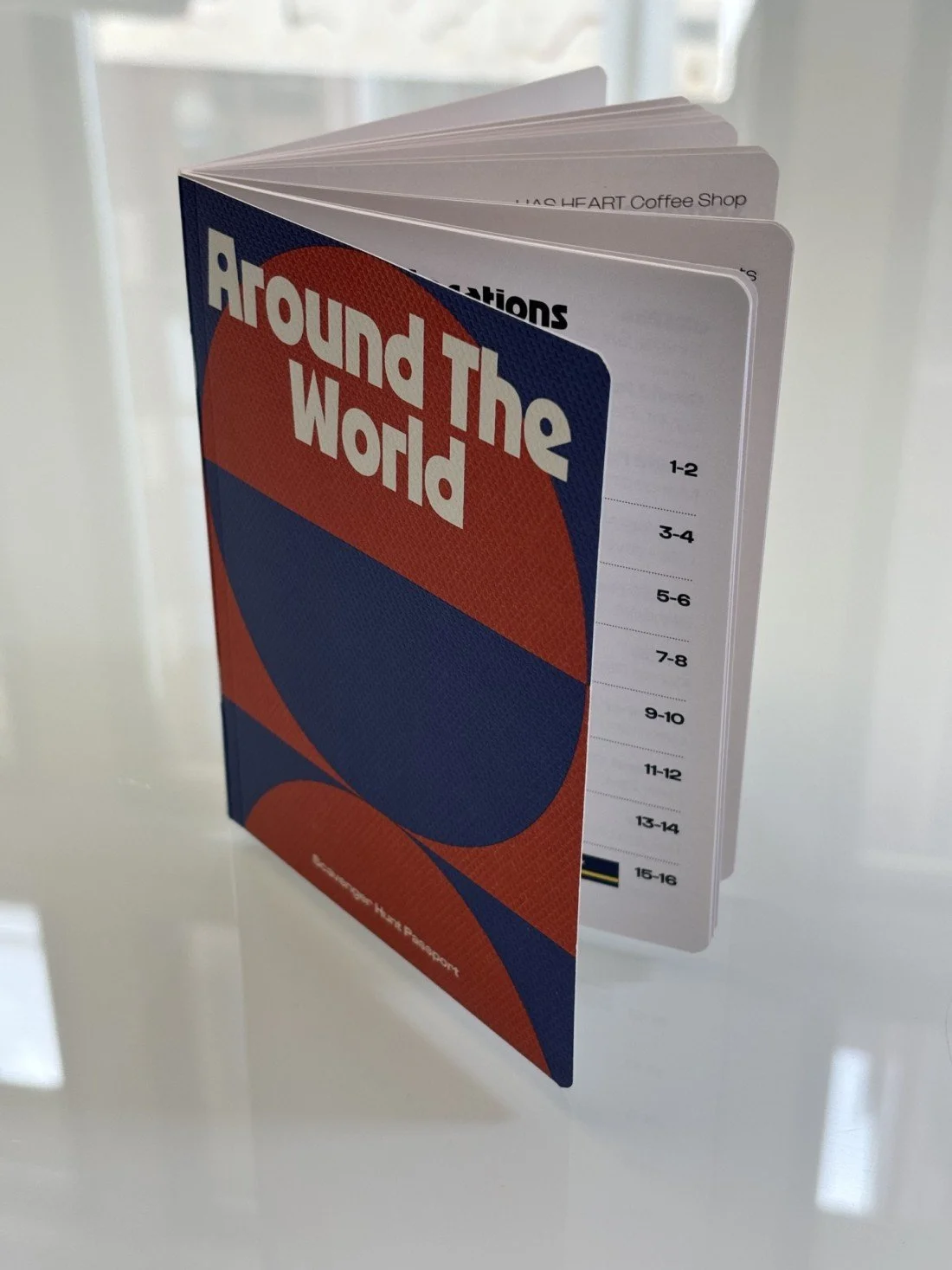 A colorful booklet titled 'Around The World' with a patterned cover, attached to a sheet with numbered sections for Downtown Grand Rapids INC's World Cup Scavenger Hunt