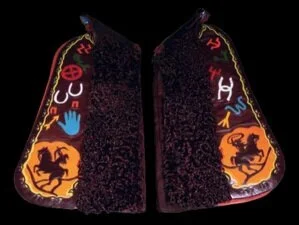 This pair of brown angora chaps captures some of our best history. The left wing features tan leather with a cowboy roping in the wing tip with old famous brands in various colors inlaid up the leg. The border is brown featuring lime green cutouts. S
