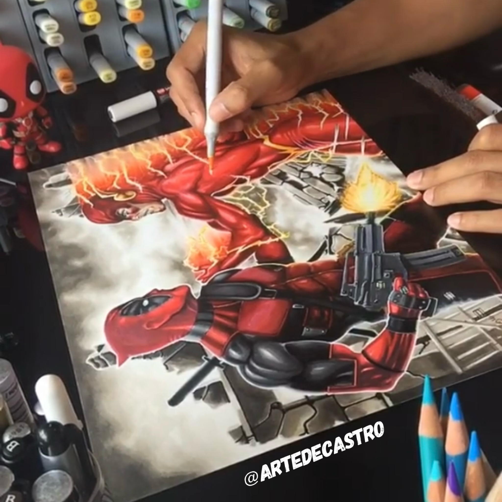 Hand writing with a white marker on a painting of a red and black superhero with lightning effects, surrounded by art supplies and colorful markers.