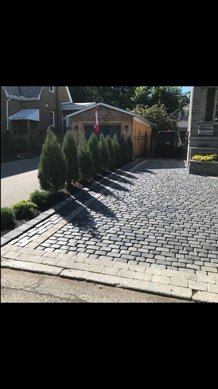 Cobblestone driveway with trees beside a wooden garage and a flag.