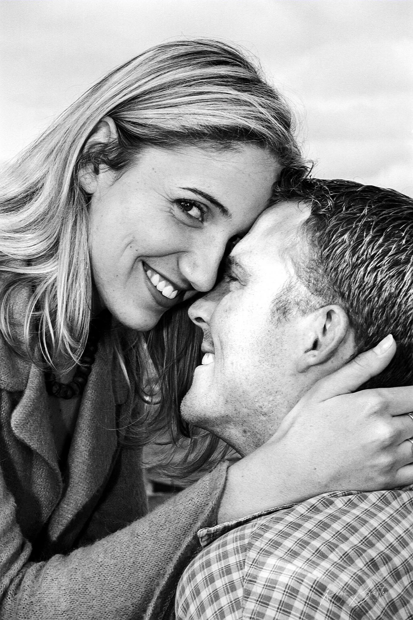 A black and white close-up photo of a woman and man smiling and touching foreheads, with the woman looking at the camera.