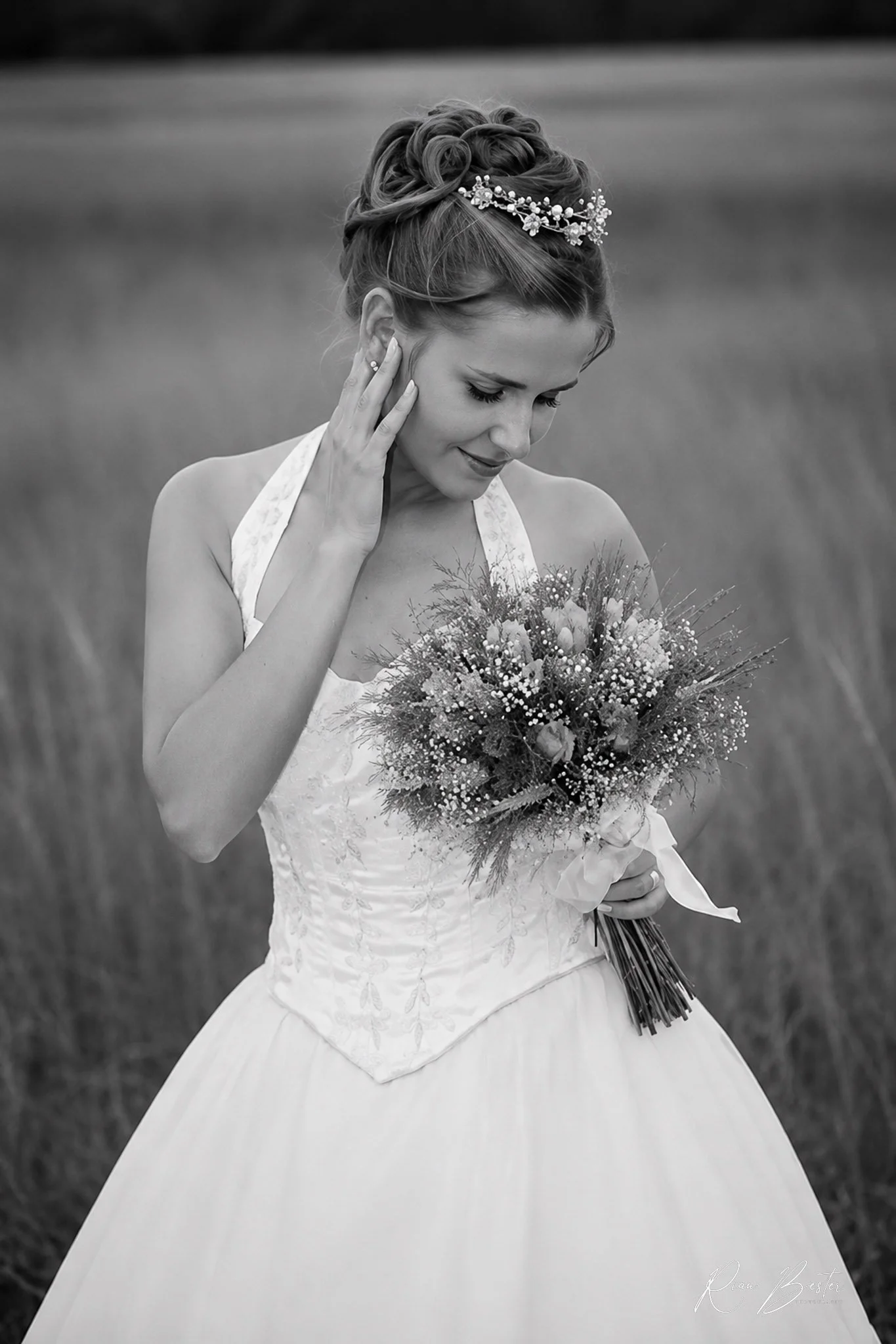 Black and white photo of a woman in a wedding dress holding a bouquet of flowers, with experiments and a soft expression, outdoors.