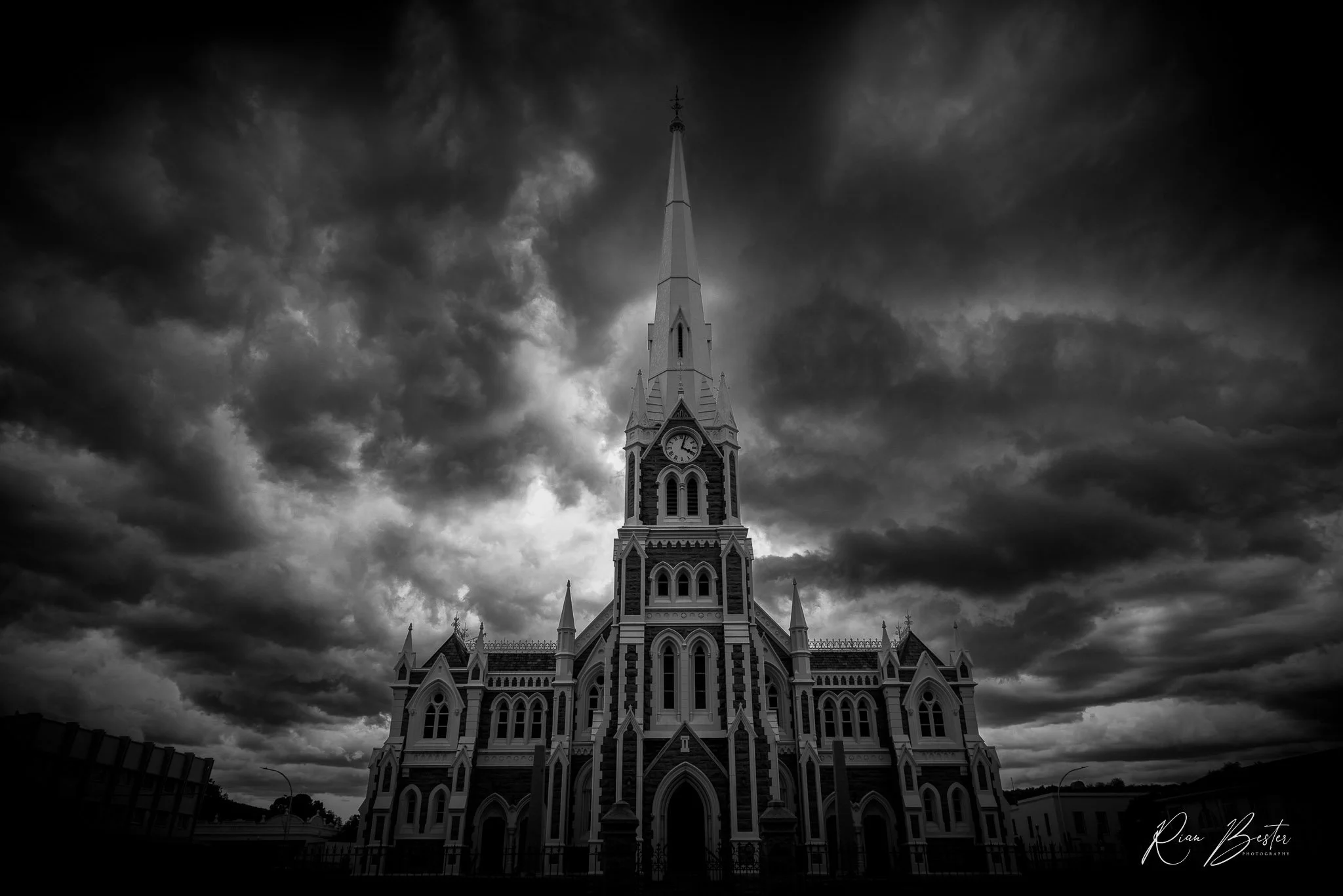 Black and white photo of a Gothic-style church with a tall steeple, under a dark, cloudy sky in Graaff-Rienet