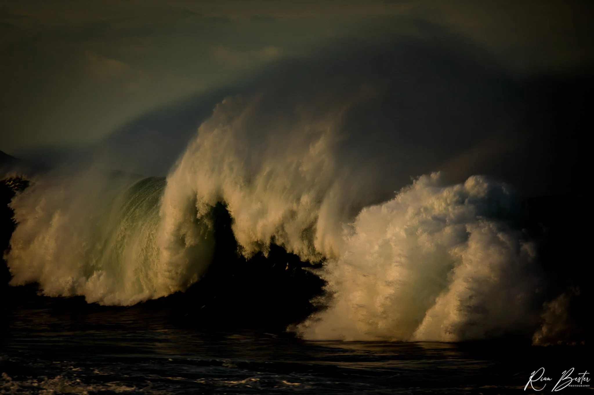 Large ocean wave crashing in a dark, stormy sea with foam and spray.