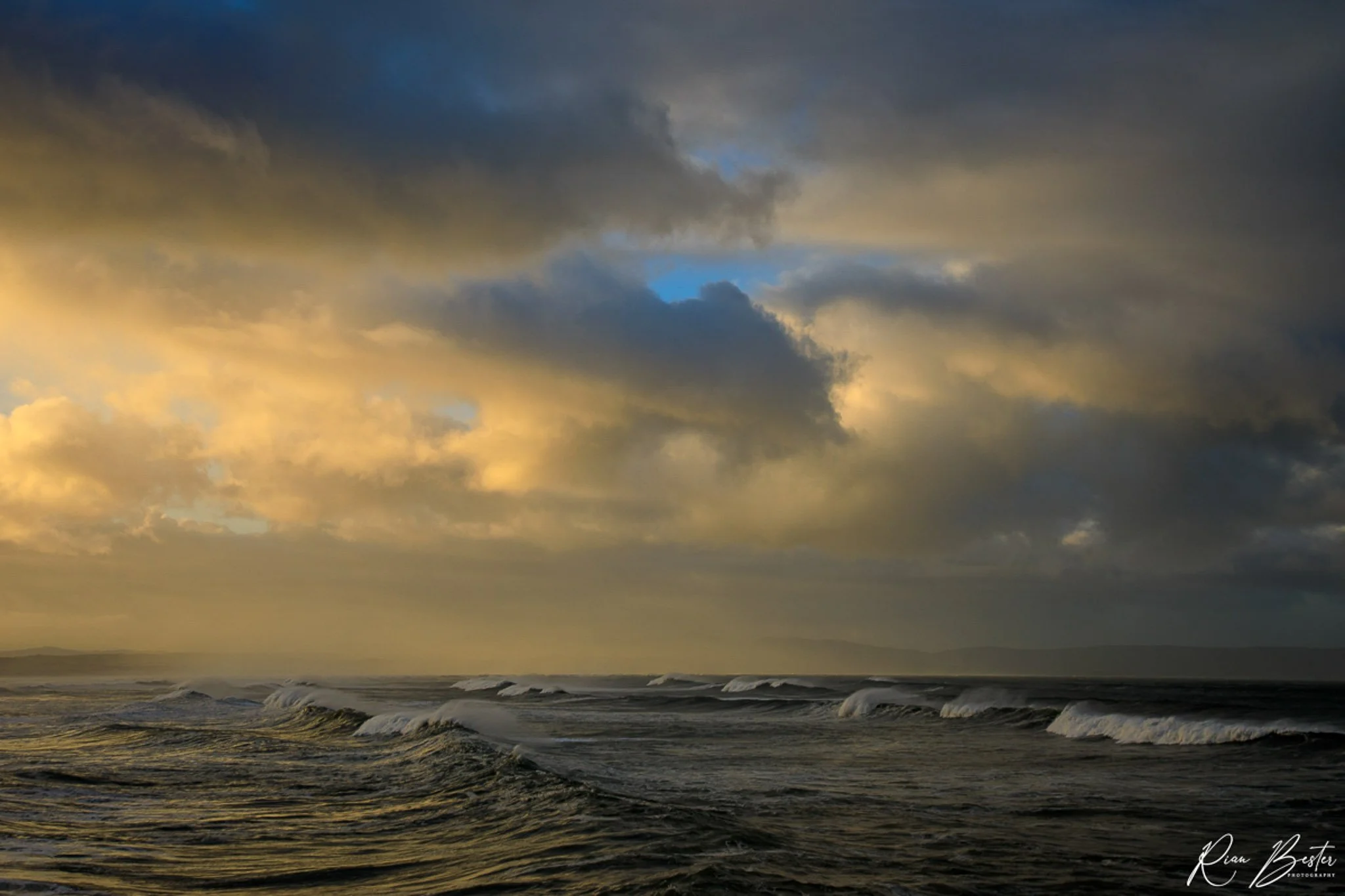 Cloudy sky over the ocean with waves, some sunlight breaking through the clouds.