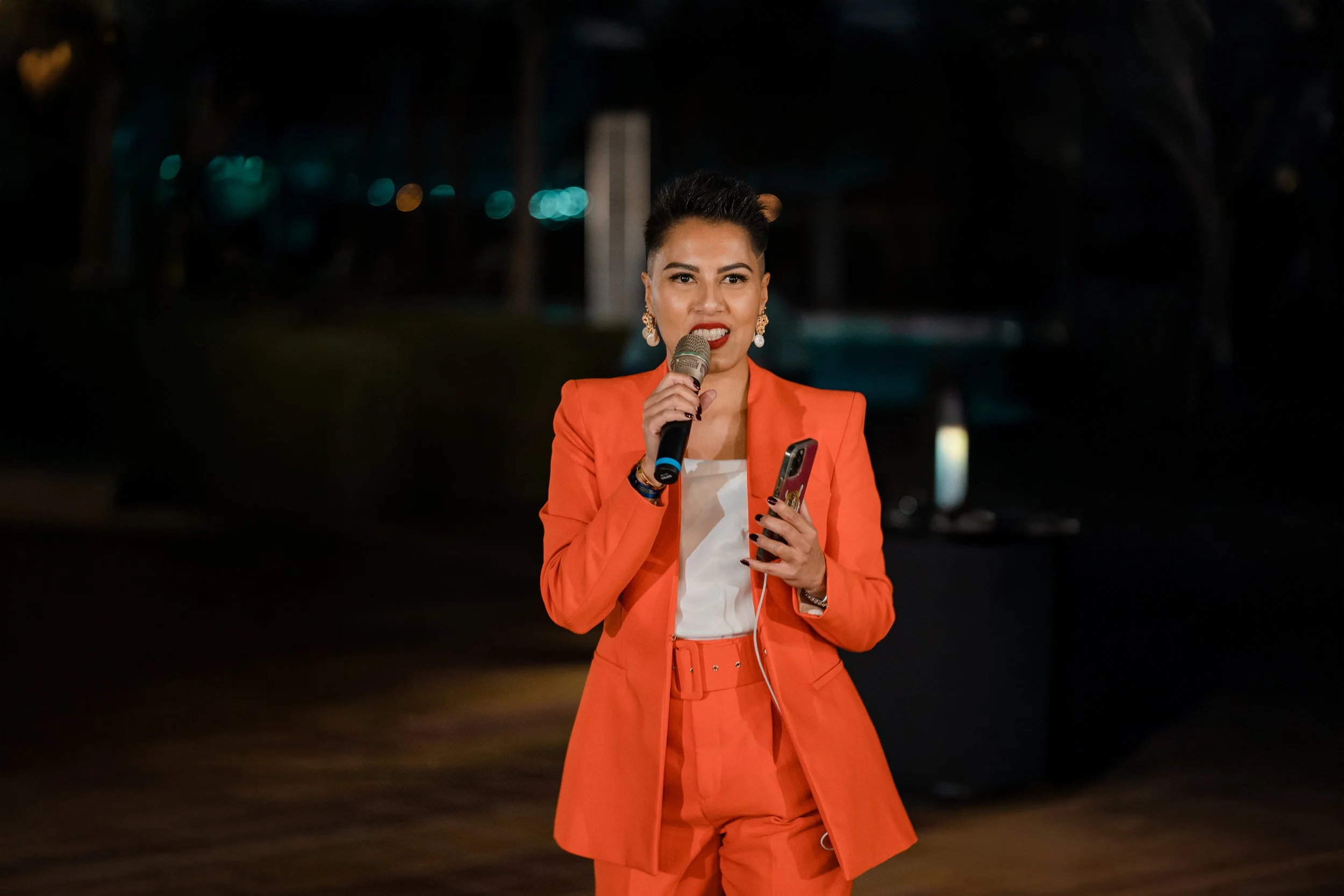 Sharon Pakir holding a microphone and addressing a large crowd on stage at an evening event in the UAE