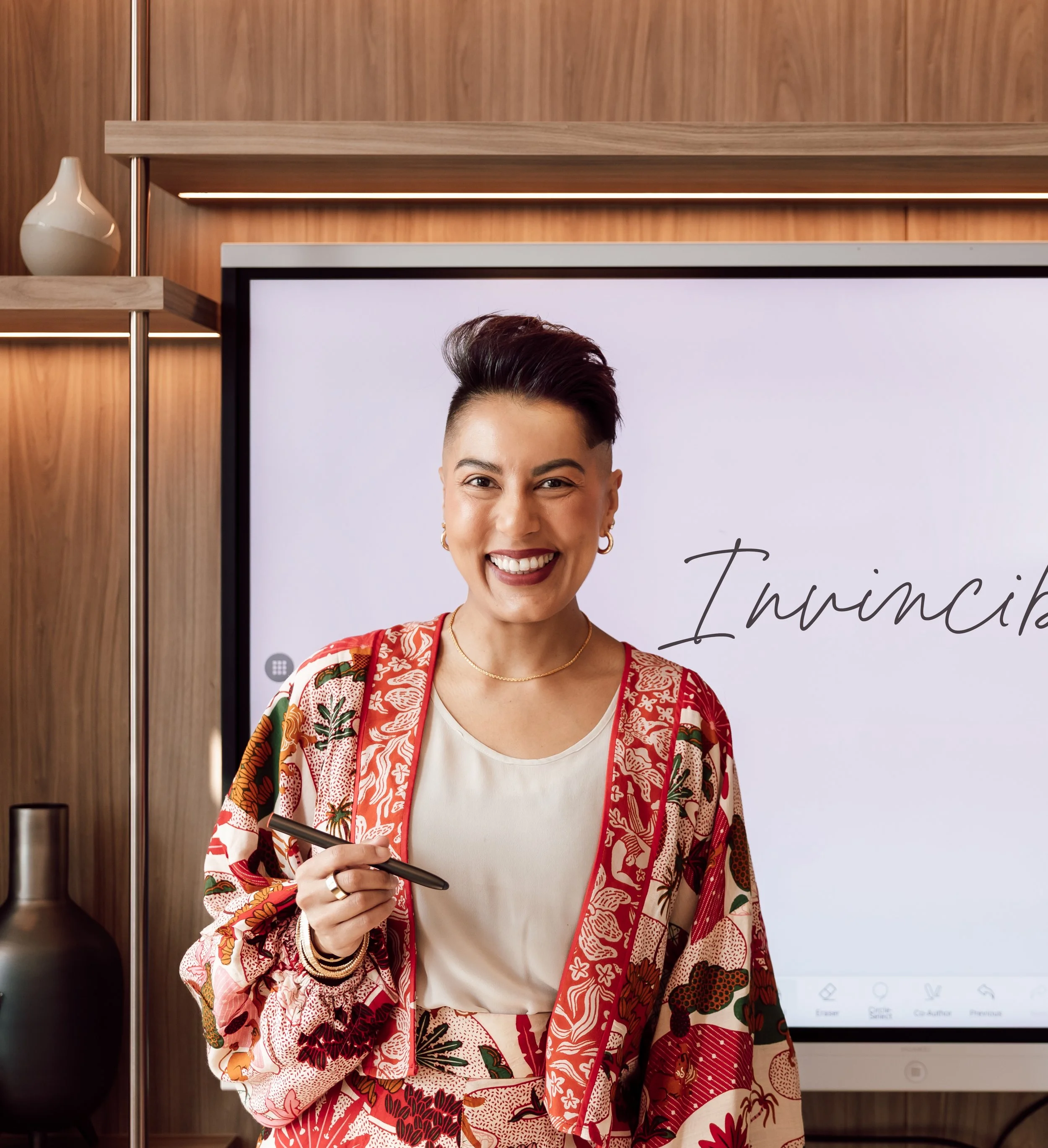 Sharon Pakir wearing a vibrant patterned suit, standing in front of a digital screen while delivering corporate leadership training in the GCC