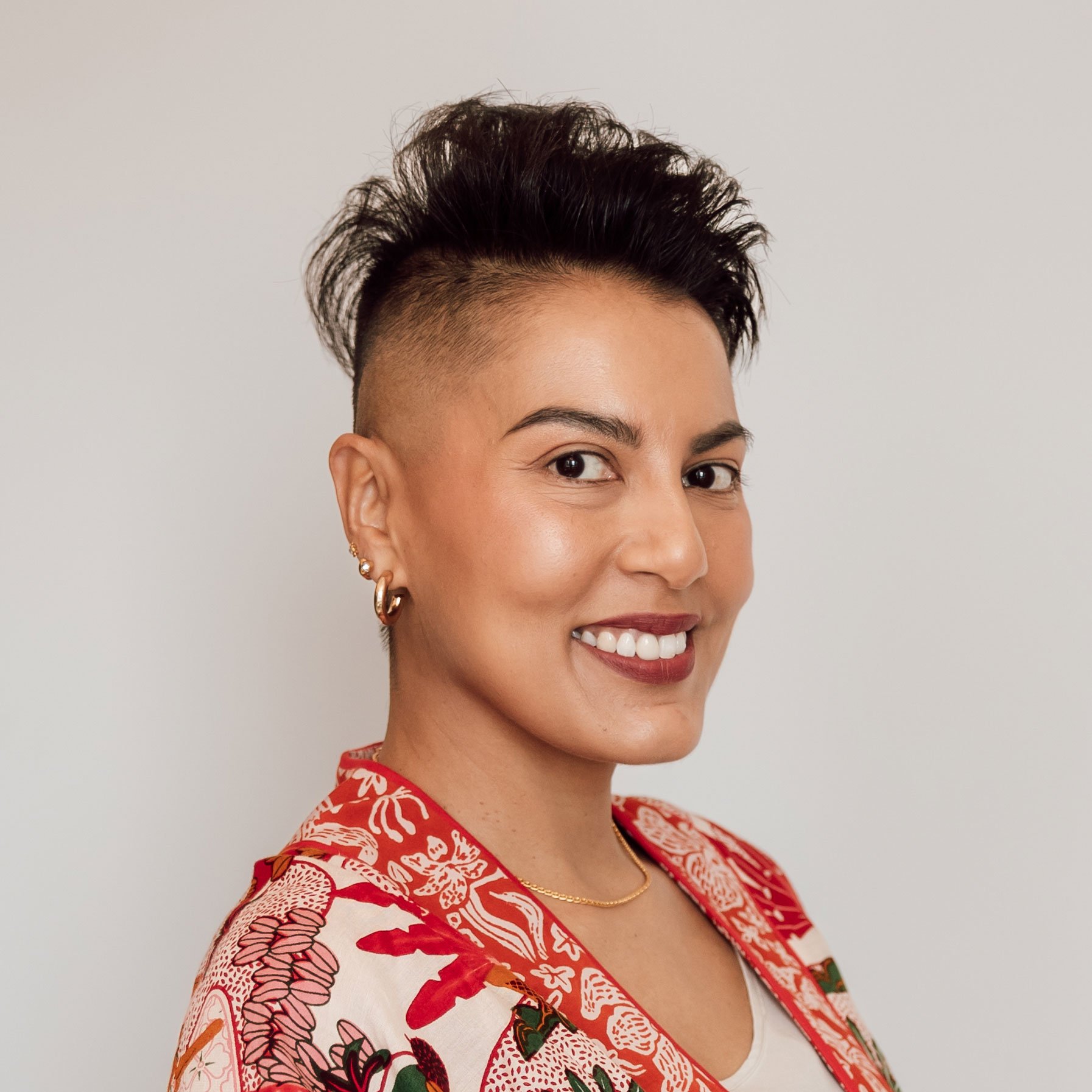 Sharon Pakir wearing a vibrant patterned suit, standing side-on and smiling at the camera