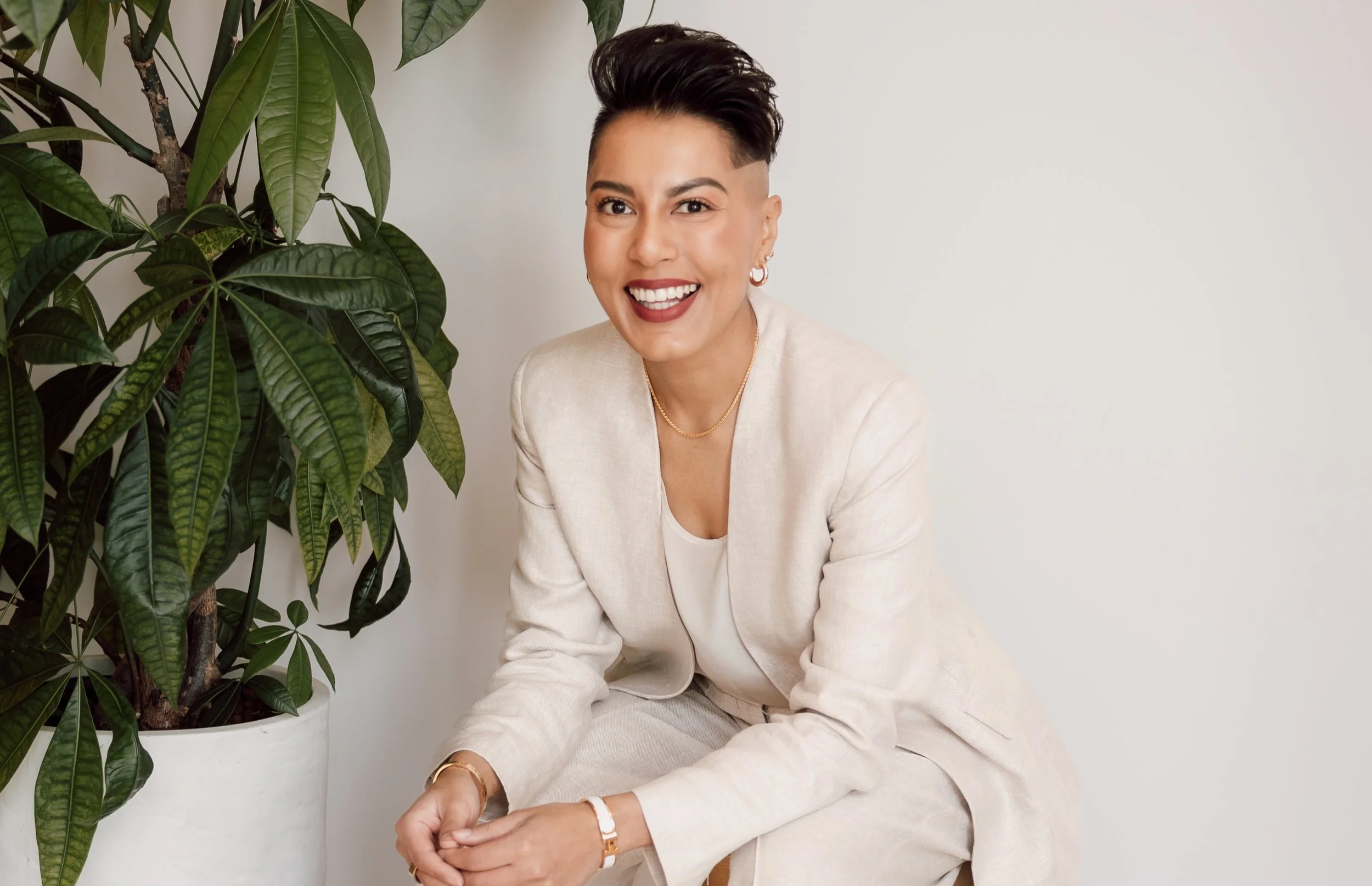 Sharon Pakir seated on a stool, leaning forward slightly and laughing