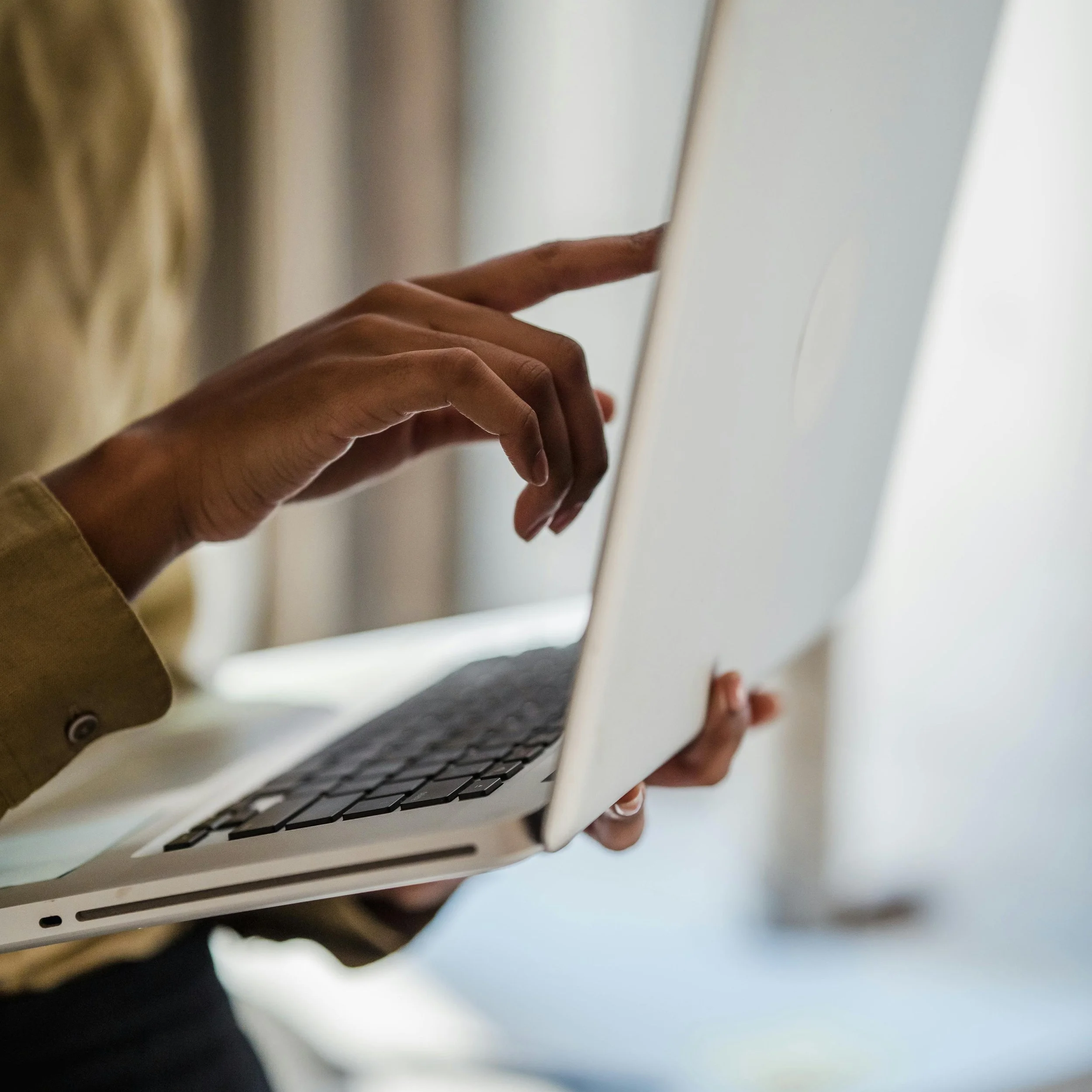 A close up photograph of a woman's hand pointing at a laptop screen showing The Invincible Co portal