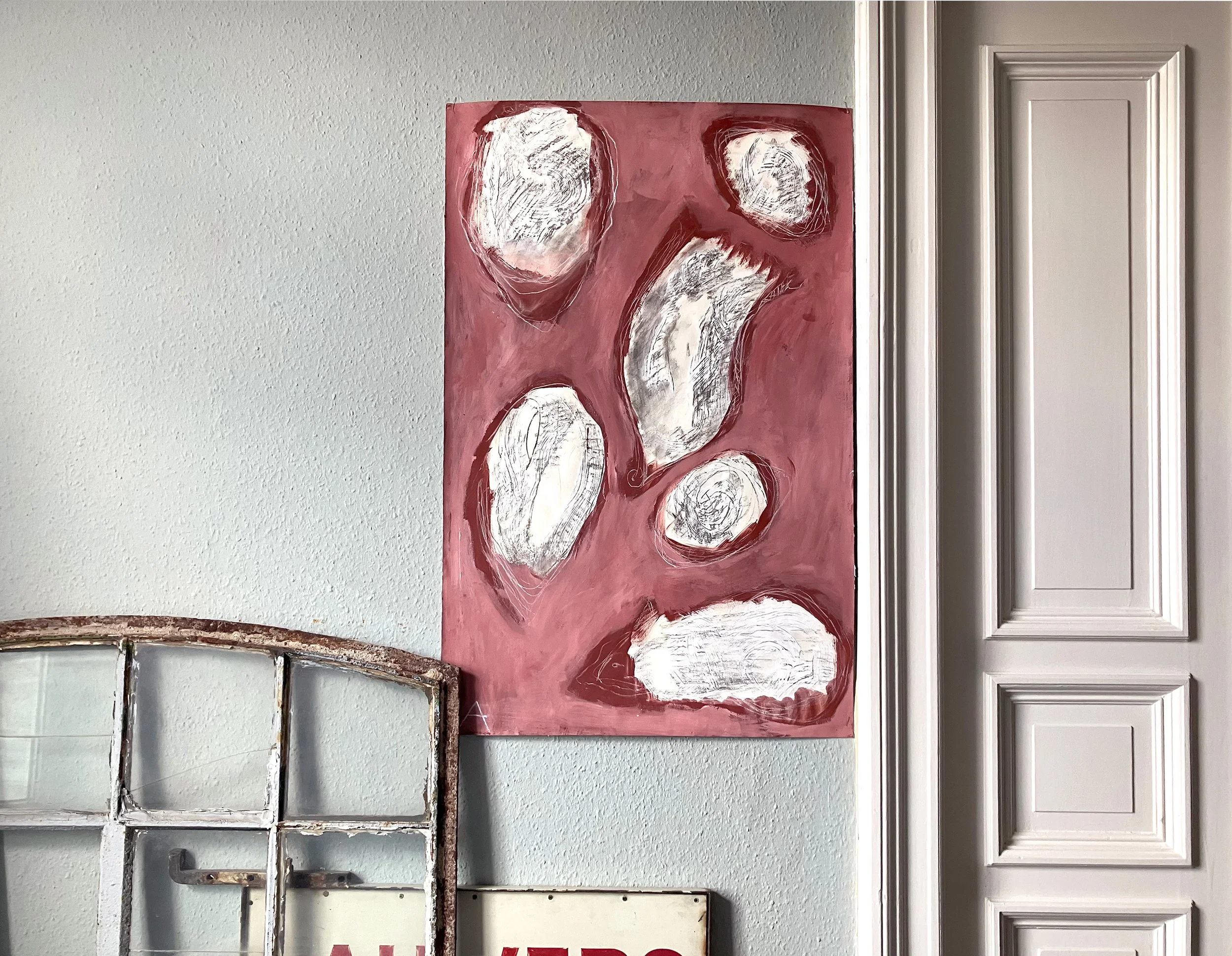 Een abstract schilderij met witte en grijze vormen op een roze achtergrond, bevestigd aan een witte muur. Een kunstwerk van Anna de Leeuw.