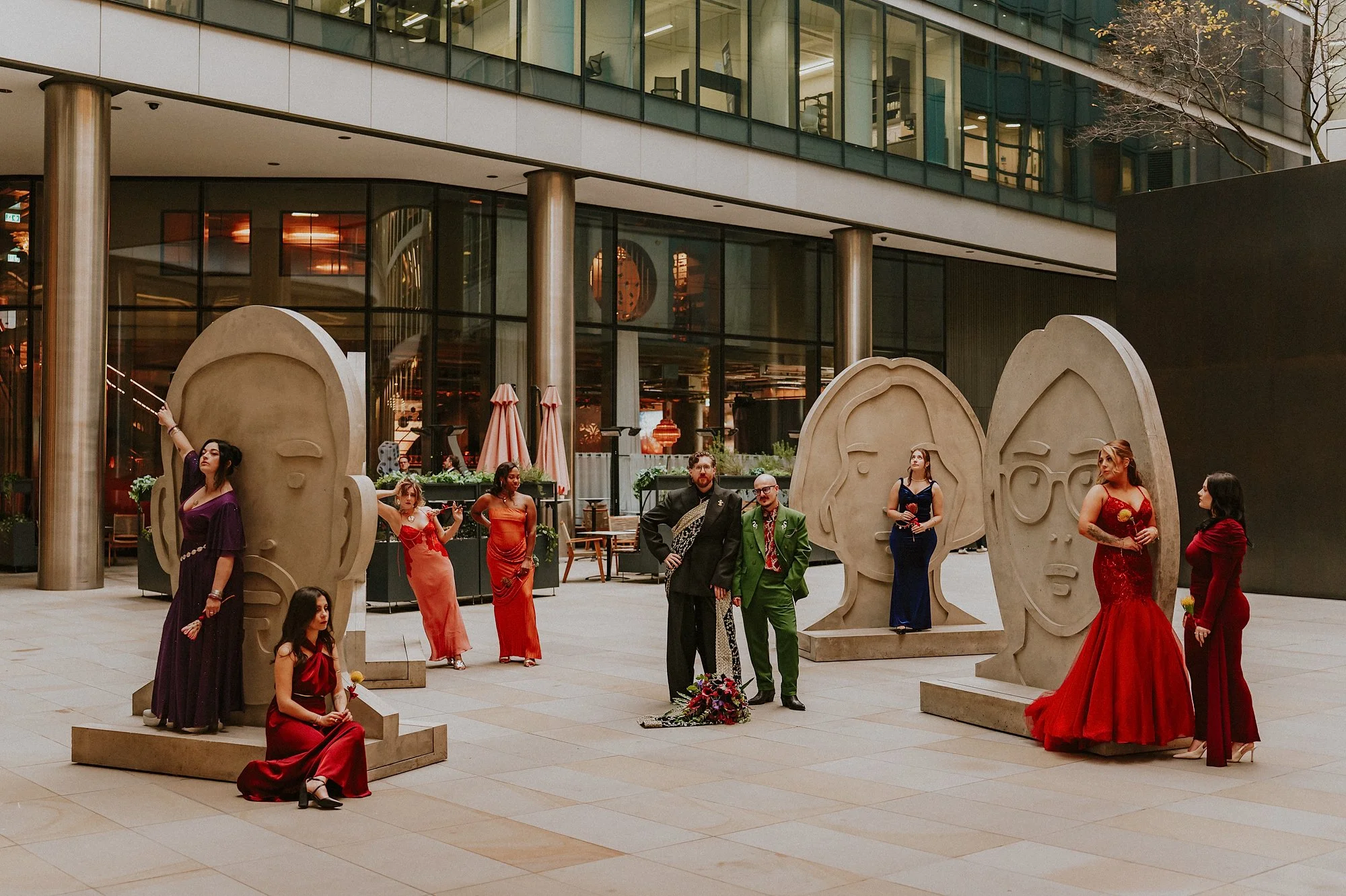 A wedding party pose next to giant head sculptures in this St Ethelburga's Centre for Reconciliation and Peace wedding in London. Concrete meets coloiur and awesome poses.