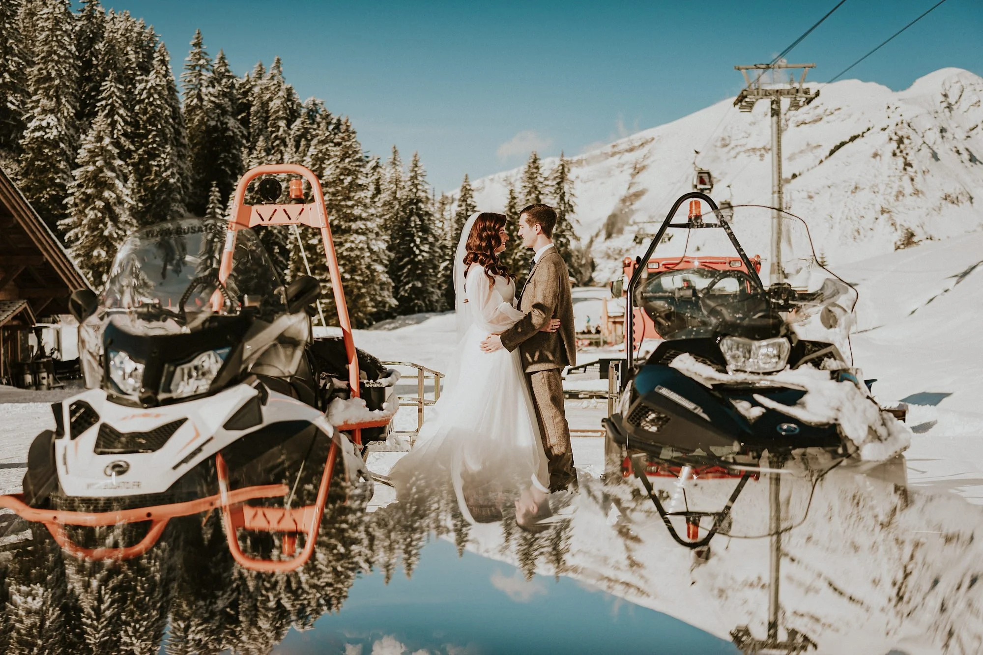 Skidoos on the French alp Ski slopes. A Bride and Groom just married embrace amidst blue skies and snow covered slopes.