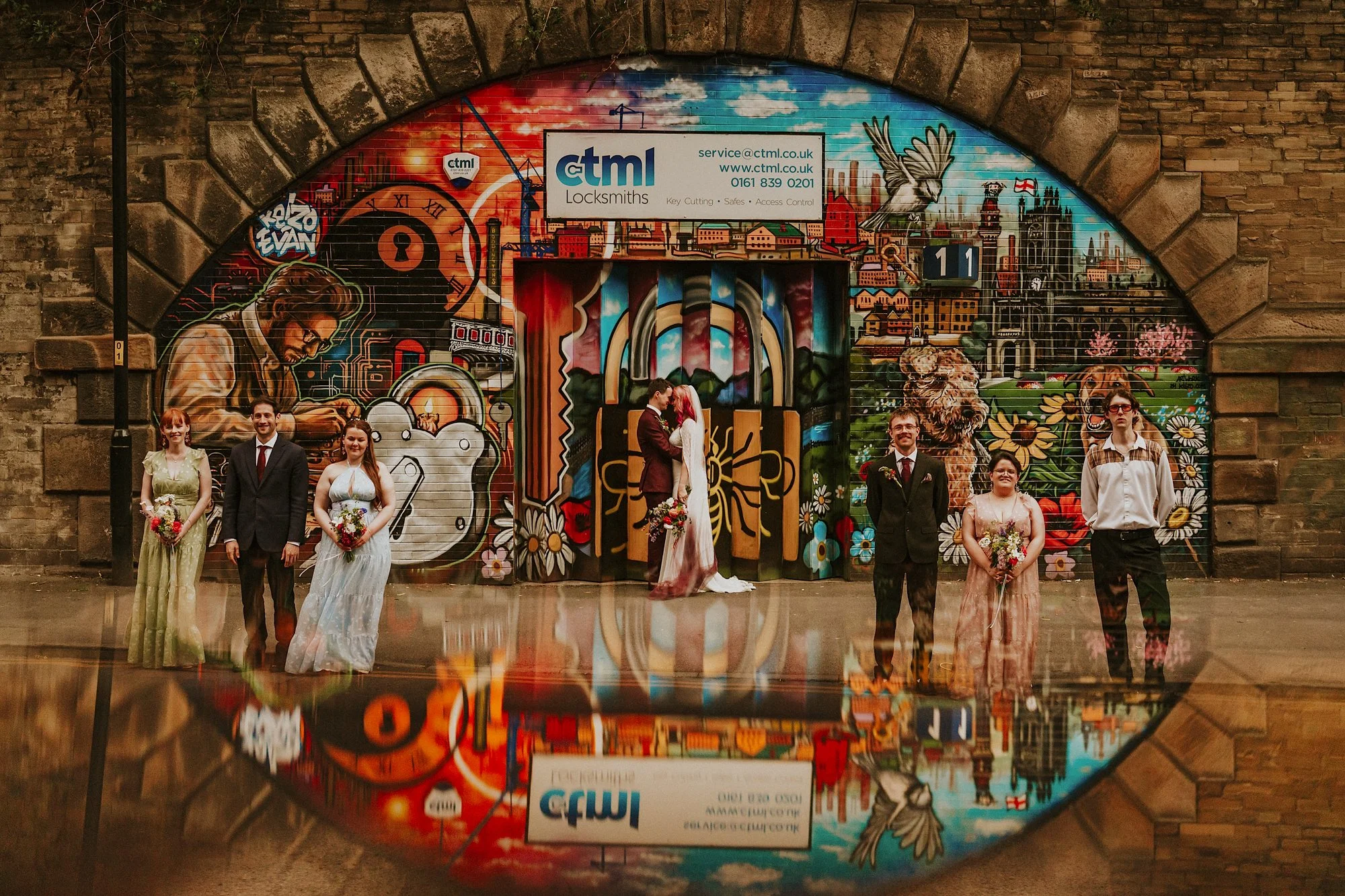 Manchester street art provide the backdrop for this Manchester wedding at Chetham's library. The wedding party pose amidst colourful street art while the couple kiss.