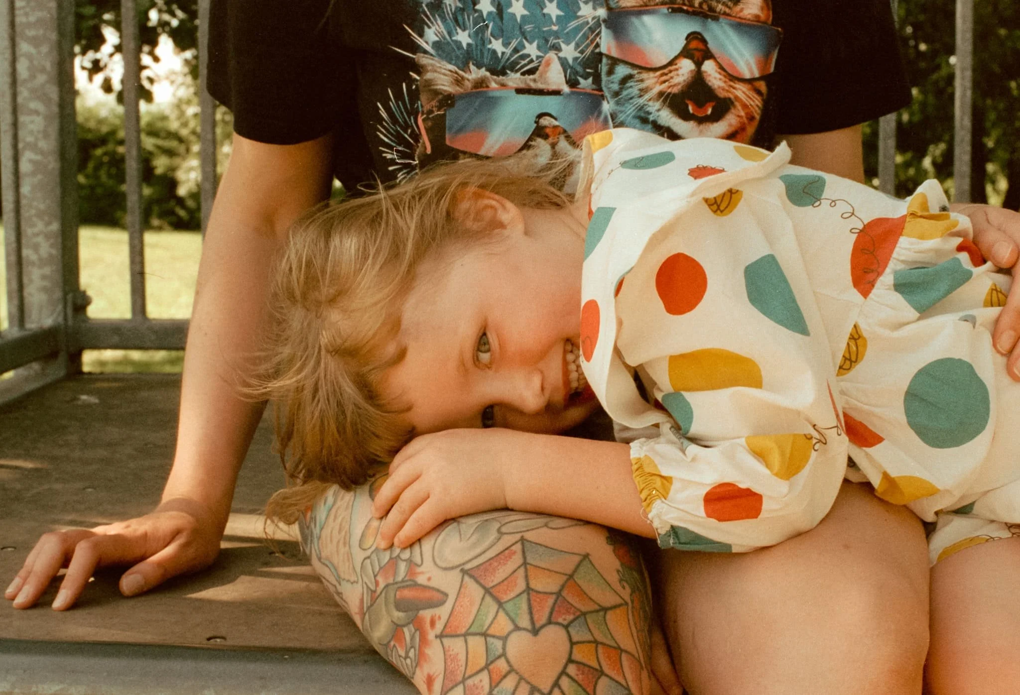 A little girl smiles as she lays on her mums knee in a skate park.