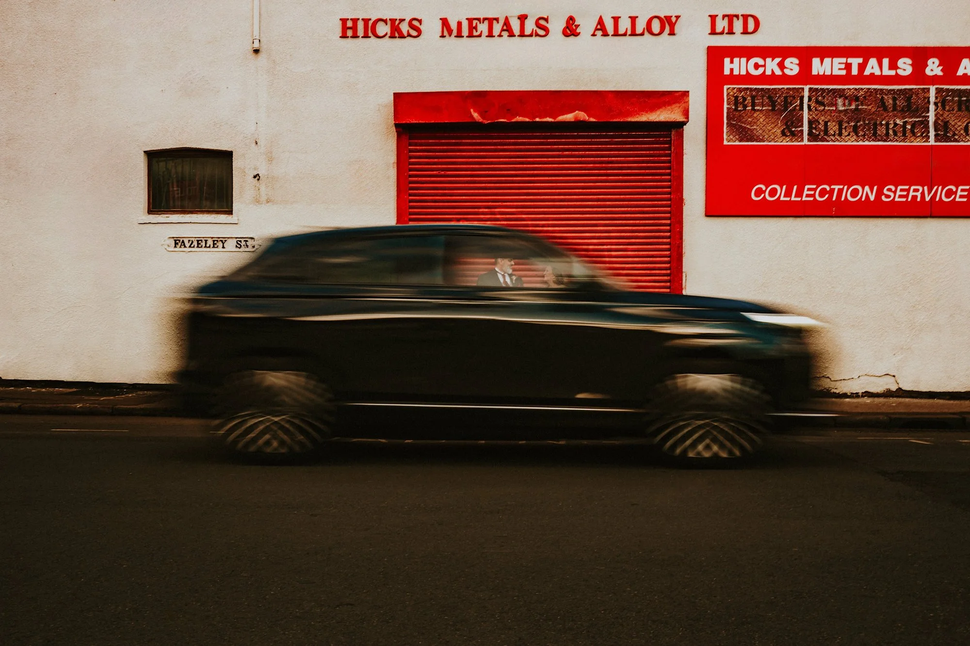 A slow shutter portrait of a Bride and Groom in their Digbeth wedding. A passing car  frames the couple in its window.