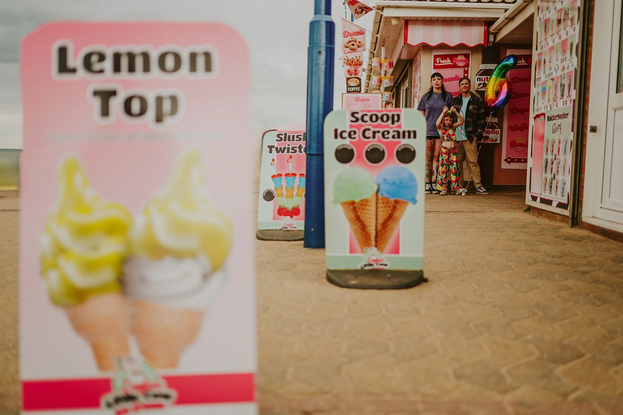 A family photoshoot on mablethorpe seafront. Holding a pink balloon in between ice cream signs. Colourful family photography at the seaside.