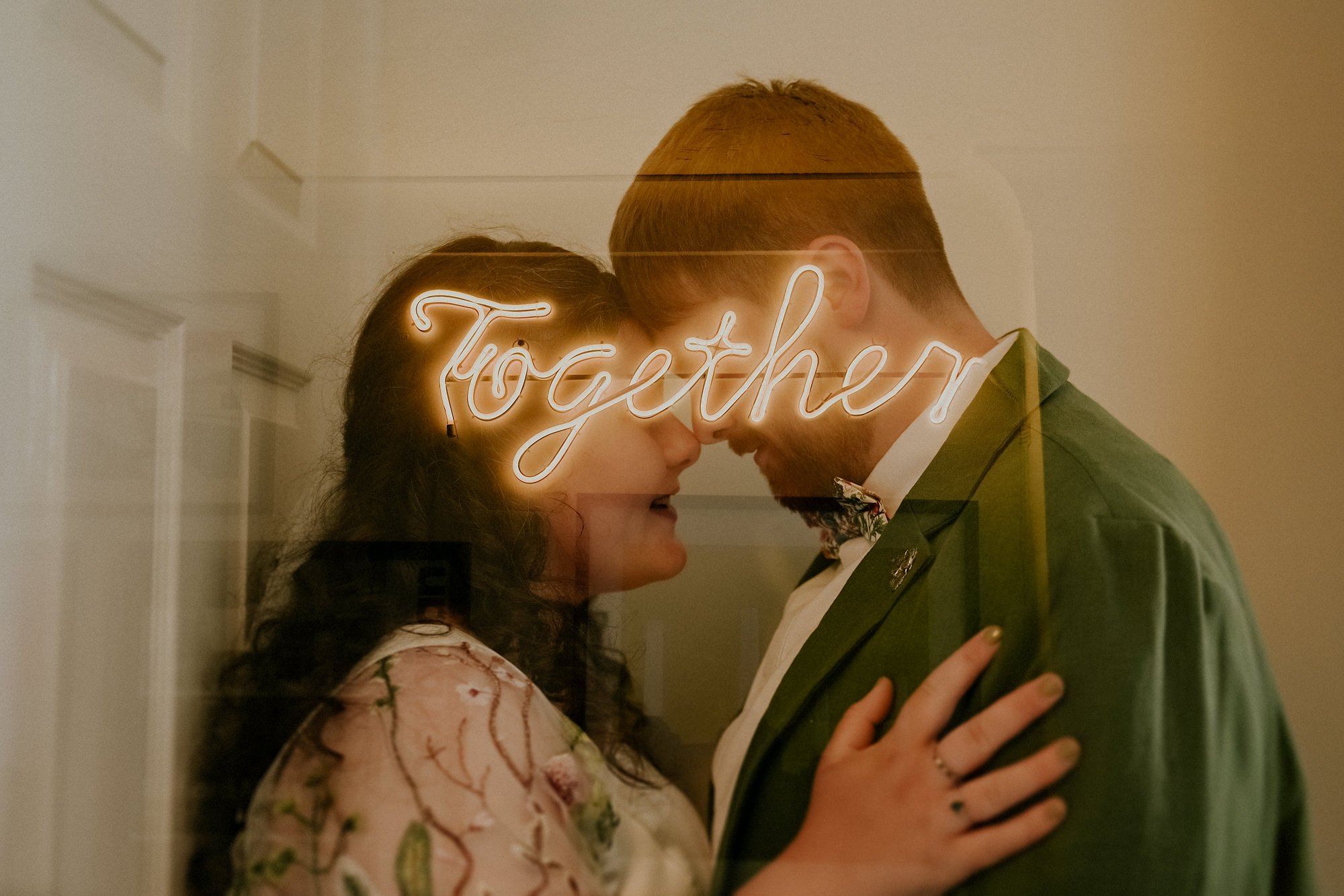 A double exposure creative portrait of a Bride and Groom face to face with a neon that reads together.