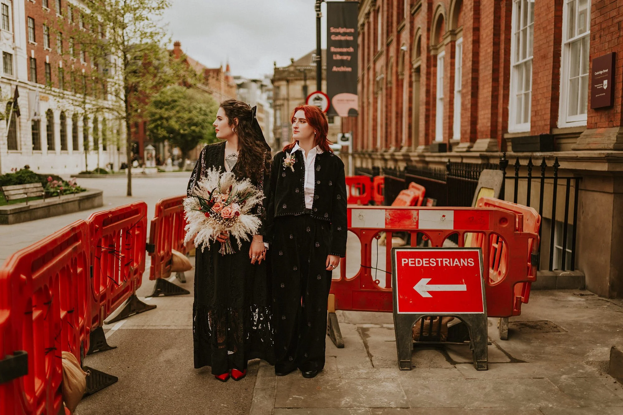 Two brides just married stand amidst road works in Leeds city centre during an atmospheric portrait in this Shears Yard wedding.