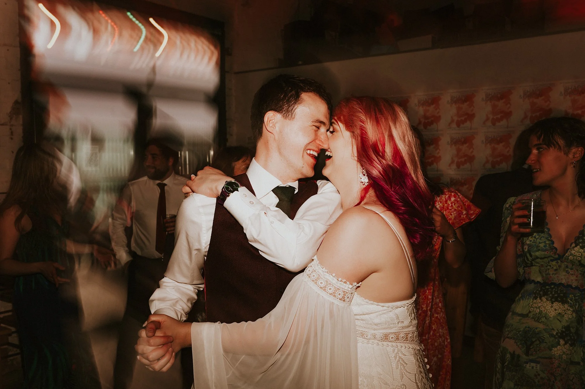 A couple share their first dance at the new cross in manchester. Both of them laugh as they embrace.