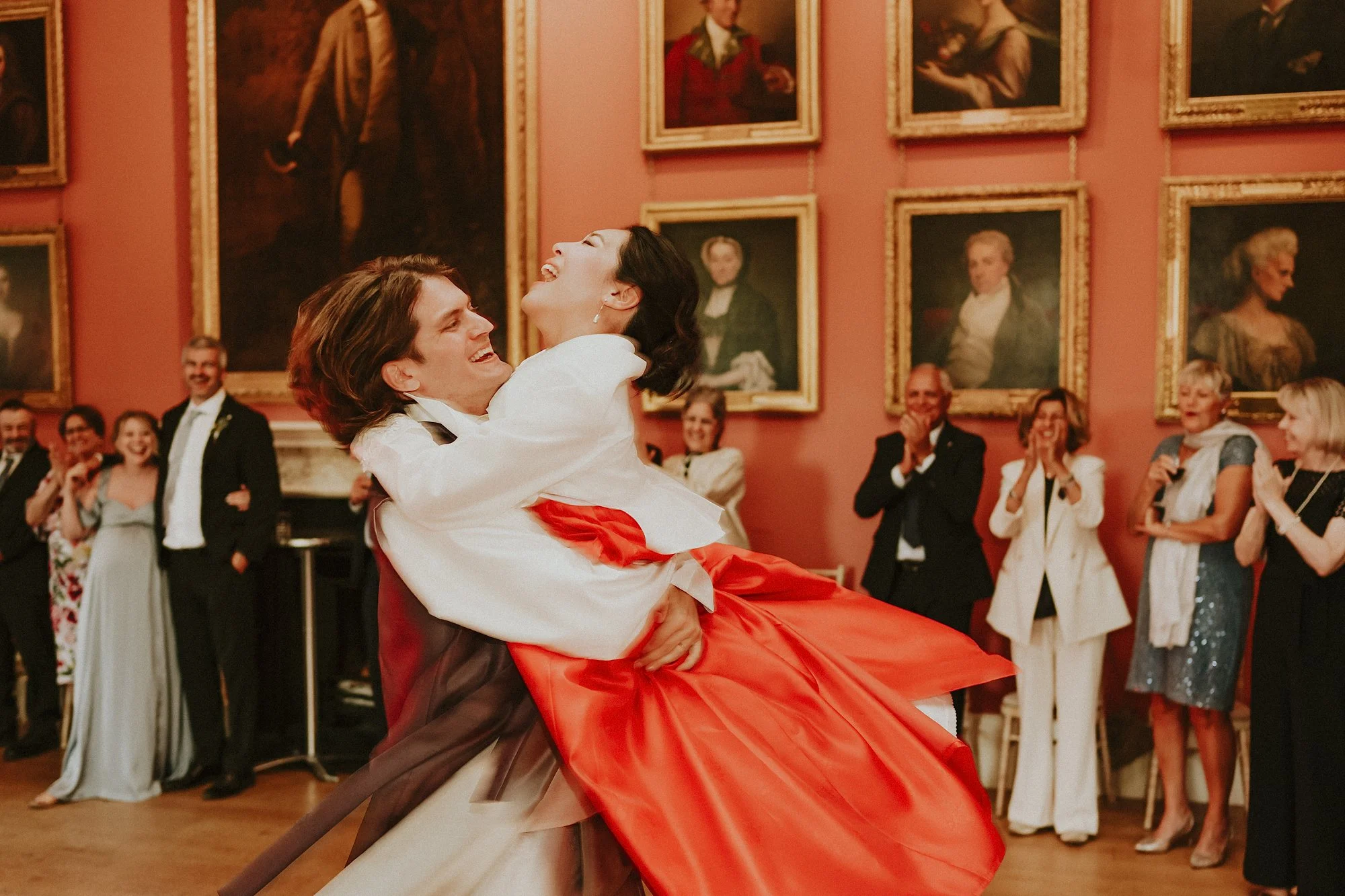 A first dance during this Winton Castle wedding. The Bride and Groom wear traditional Korean dress as he spins her romantically while people look on.