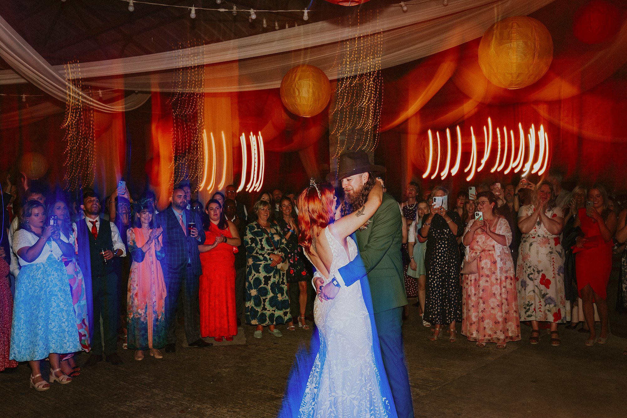 A first dance inside White Syke fields wedding barn. A couple dance amidst colourful lights as those they love most watch on.