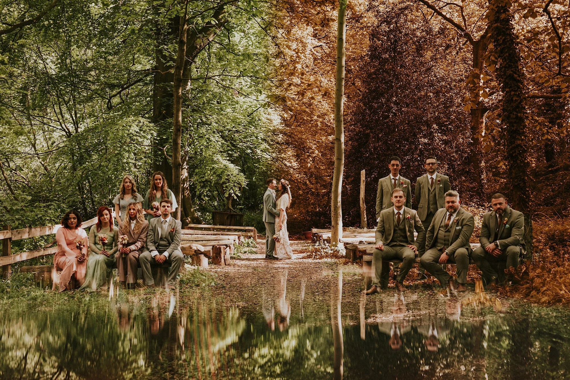 A wedding party portrait at this green moon. Surrounded by forest the couple embrace while the wedding party sit and look into the camera. The scene is split into Summer & Autumn. Nature embraces this sustainable wedding in Leeds.