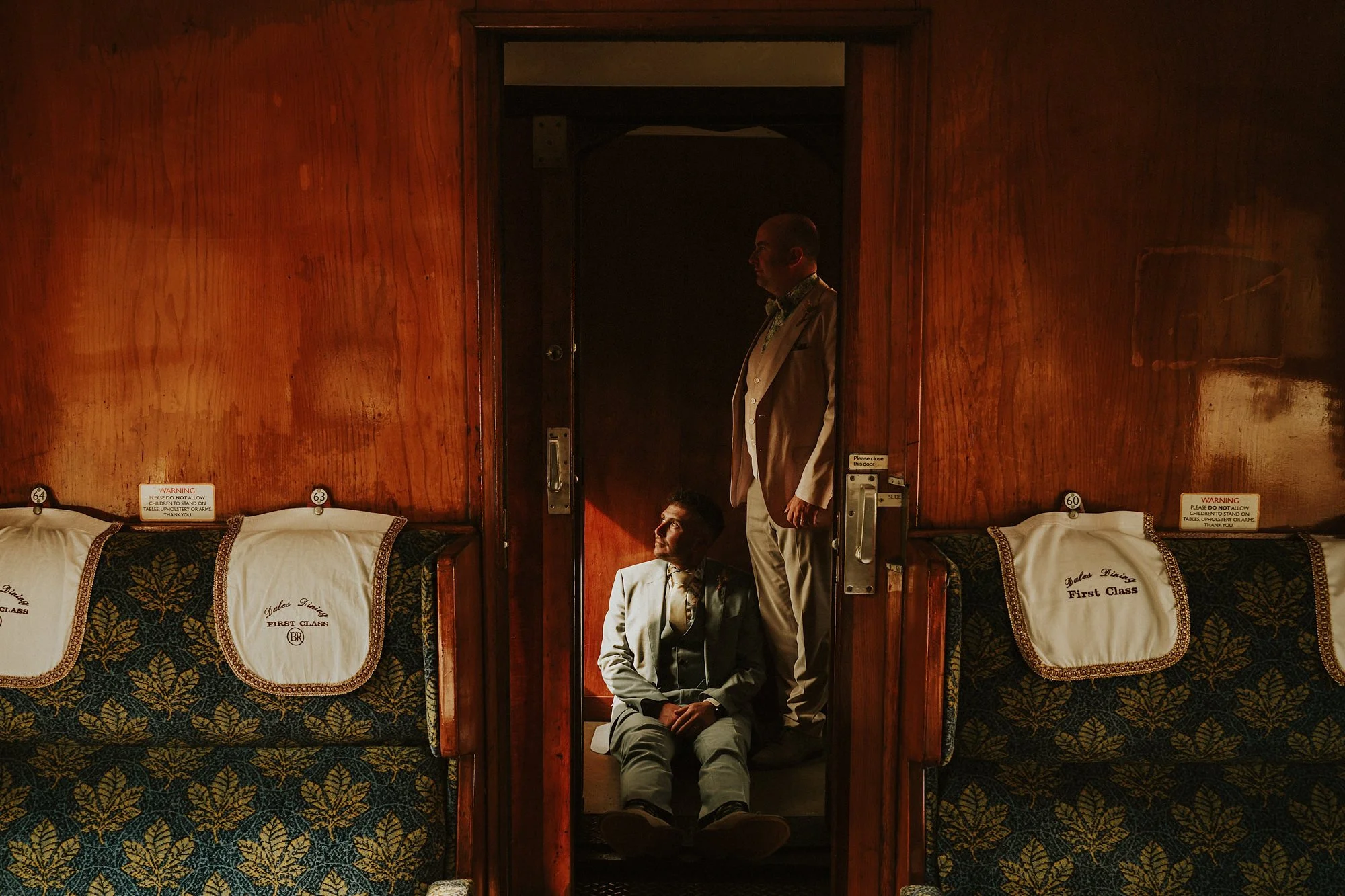 Two grooms during their wedding on a steam train in the first class carriage. Mahogany & train seats frame this atmospheric portrait.