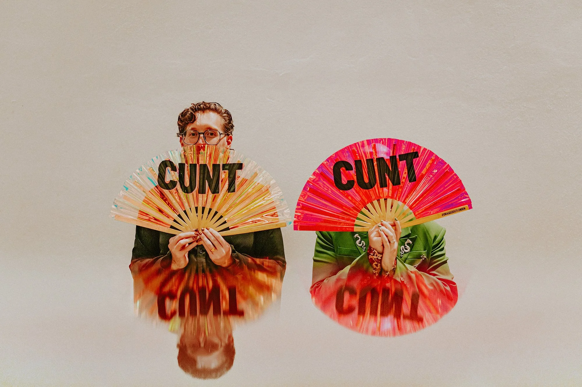 A reflection image of two grooms in a same sex wedding at St Ethelburga's Centre for Reconciliation and Peace. The two grooms hold fans reading expletives.