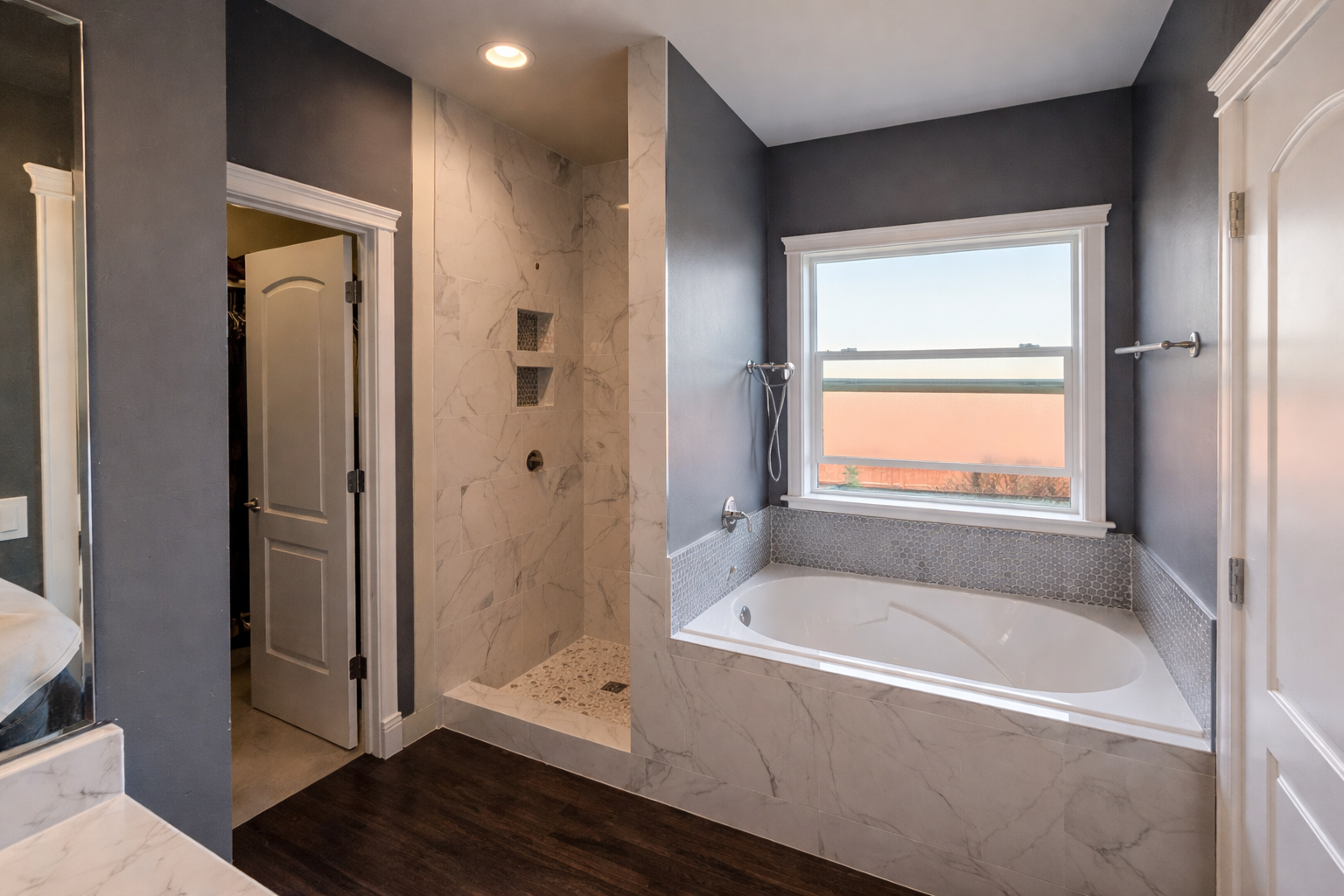 Bathroom with a walk-in shower, a bathtub under a large window, dark blue walls, white marble accents, and a closed door leading to a closet.