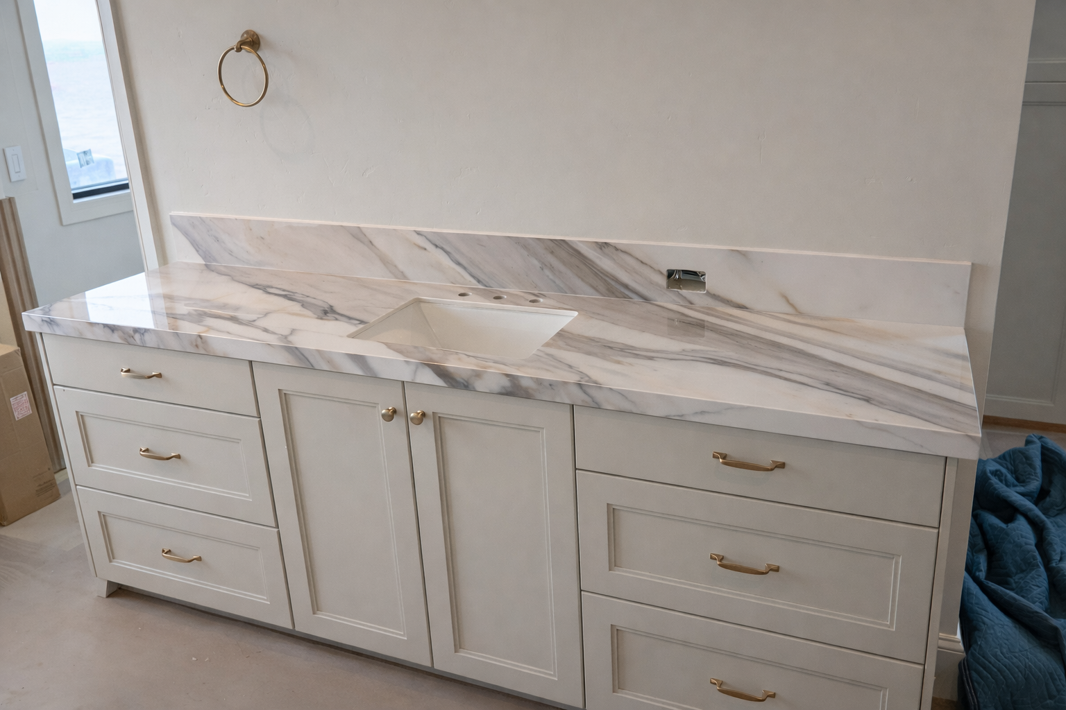 White kitchen cabinet with gold handles and a marble countertop with a built-in sink.